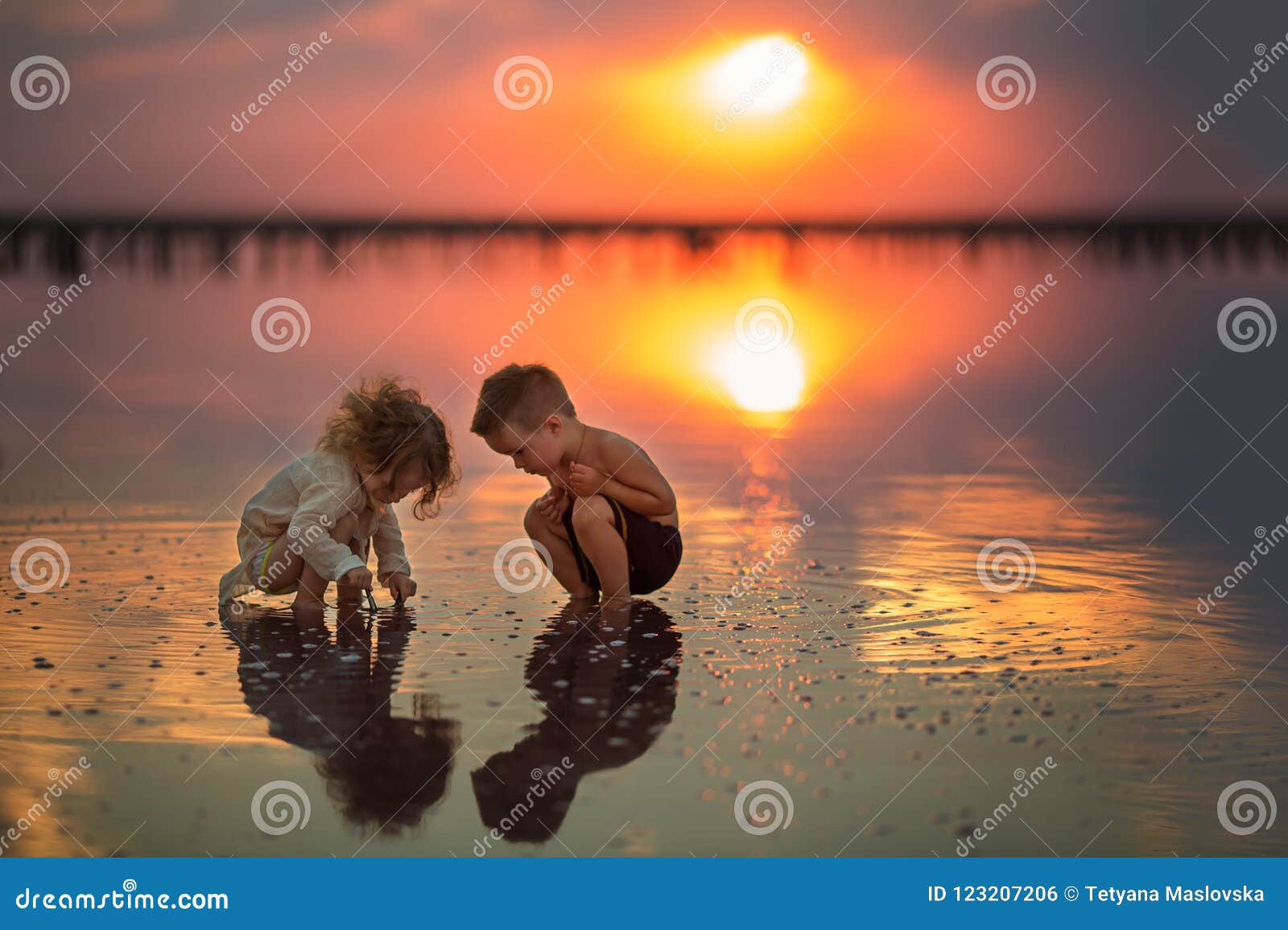 I bambini mangiano le mele nella cucina alla mattina La sorella ed il fratello tengono la mela nel loro piccolo gioco dei bambini. Due piccoli bambini che giocano sulla spiaggia durante il tramonto Riflessione in acqua