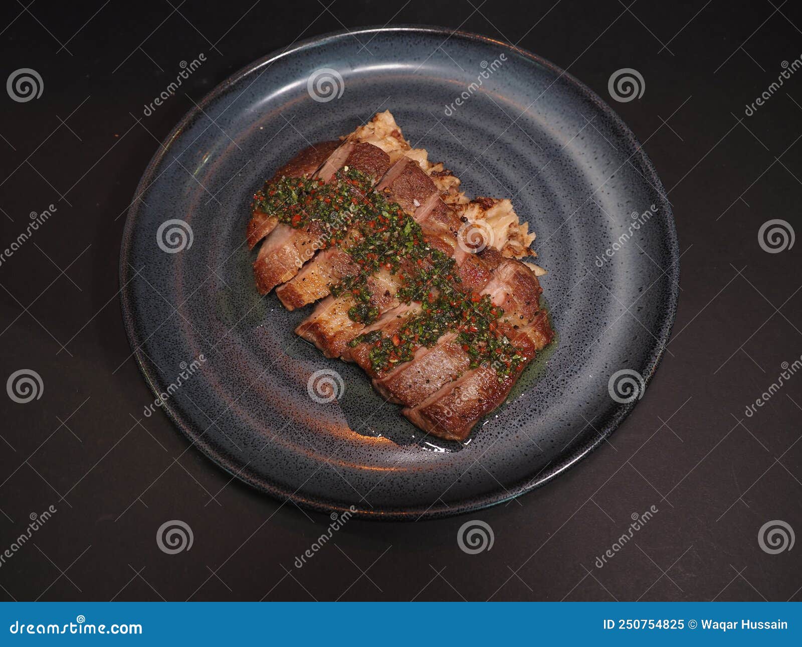 iberico pork collar steak with chimichurri served in a dish  on dark background top view