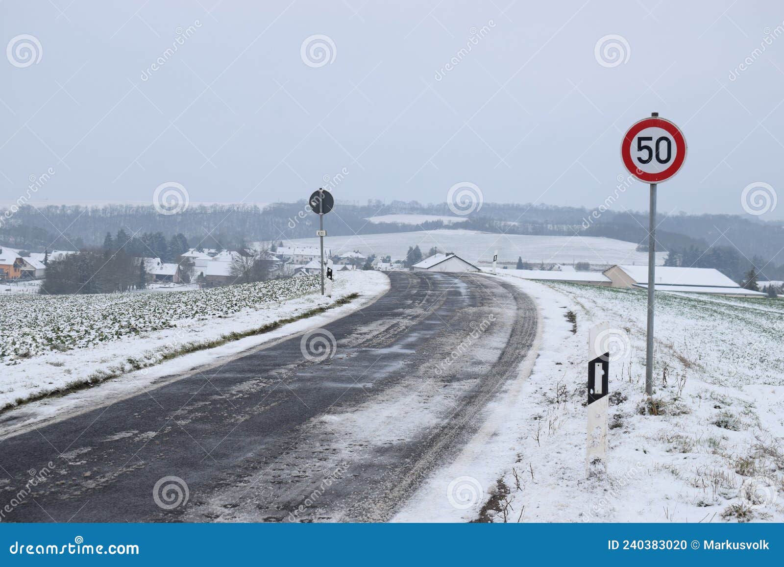 icy road into snowy village welling in the valley, speed limit 50 sign on the hill already