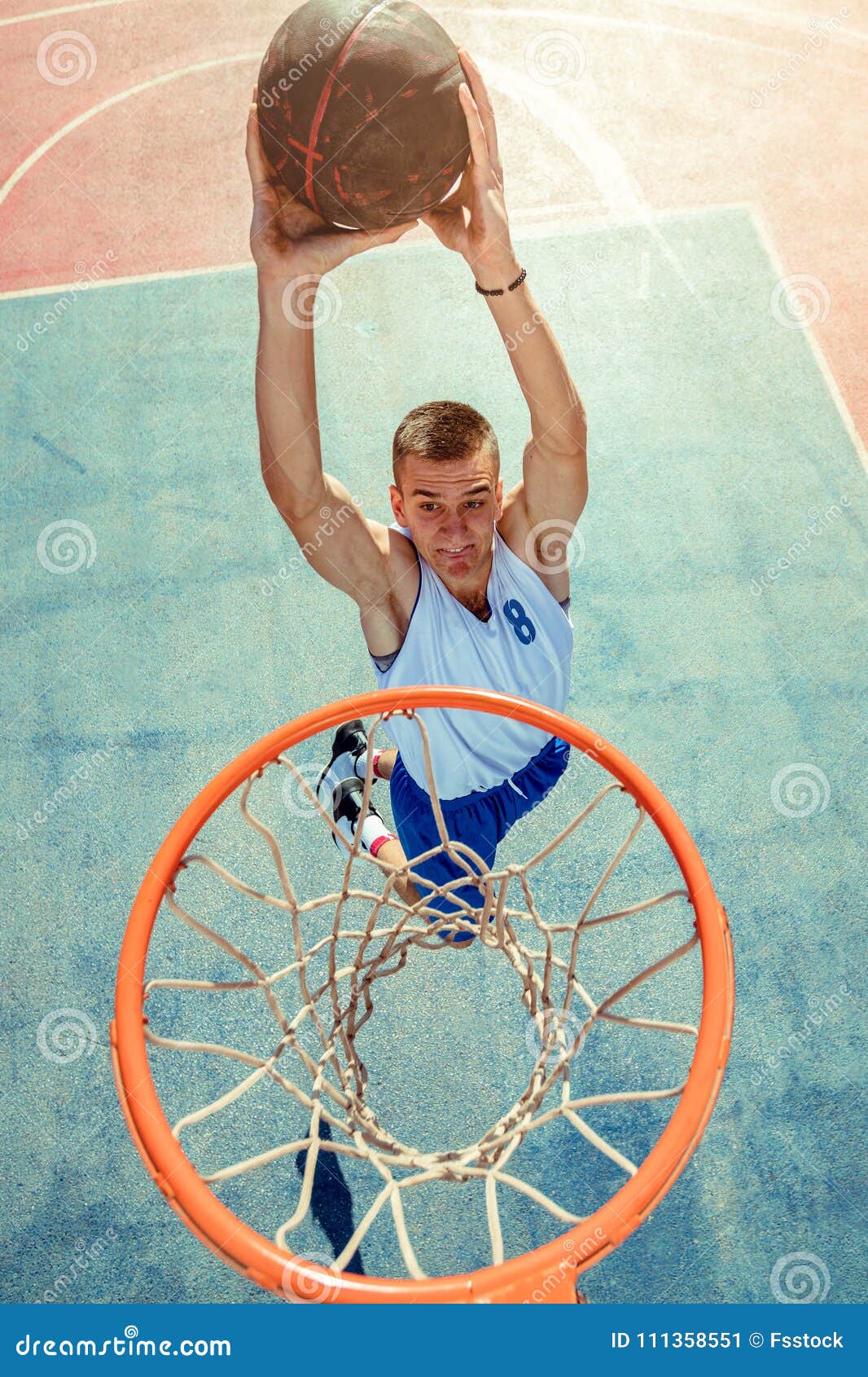 Ângulo baixo do jogador de streetball masculino mirando com bola enquanto  jogava basquete contra o céu azul