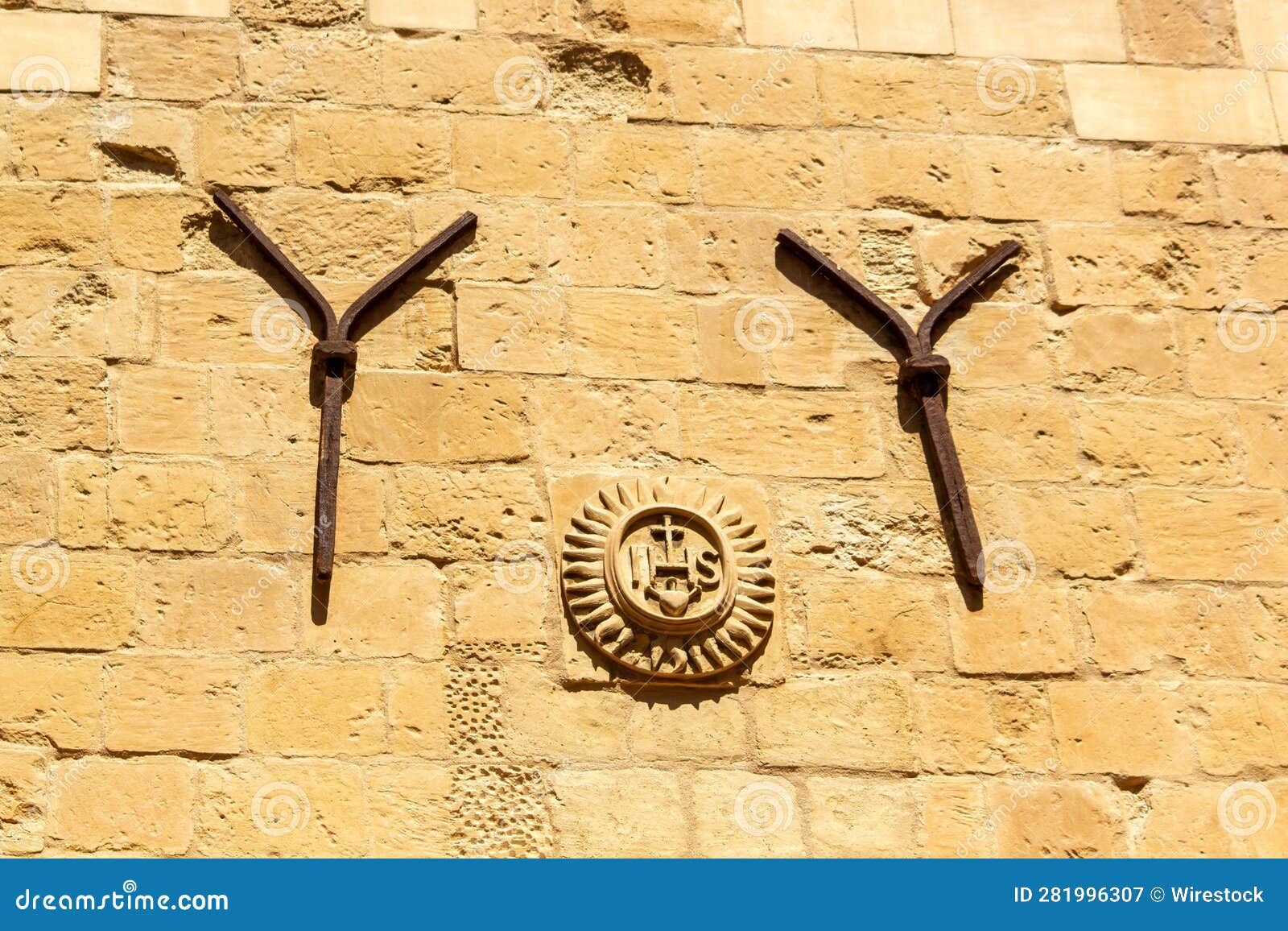 ihs stone emblem and two iron y s decorating the back of the jesuits church. valletta, malta.