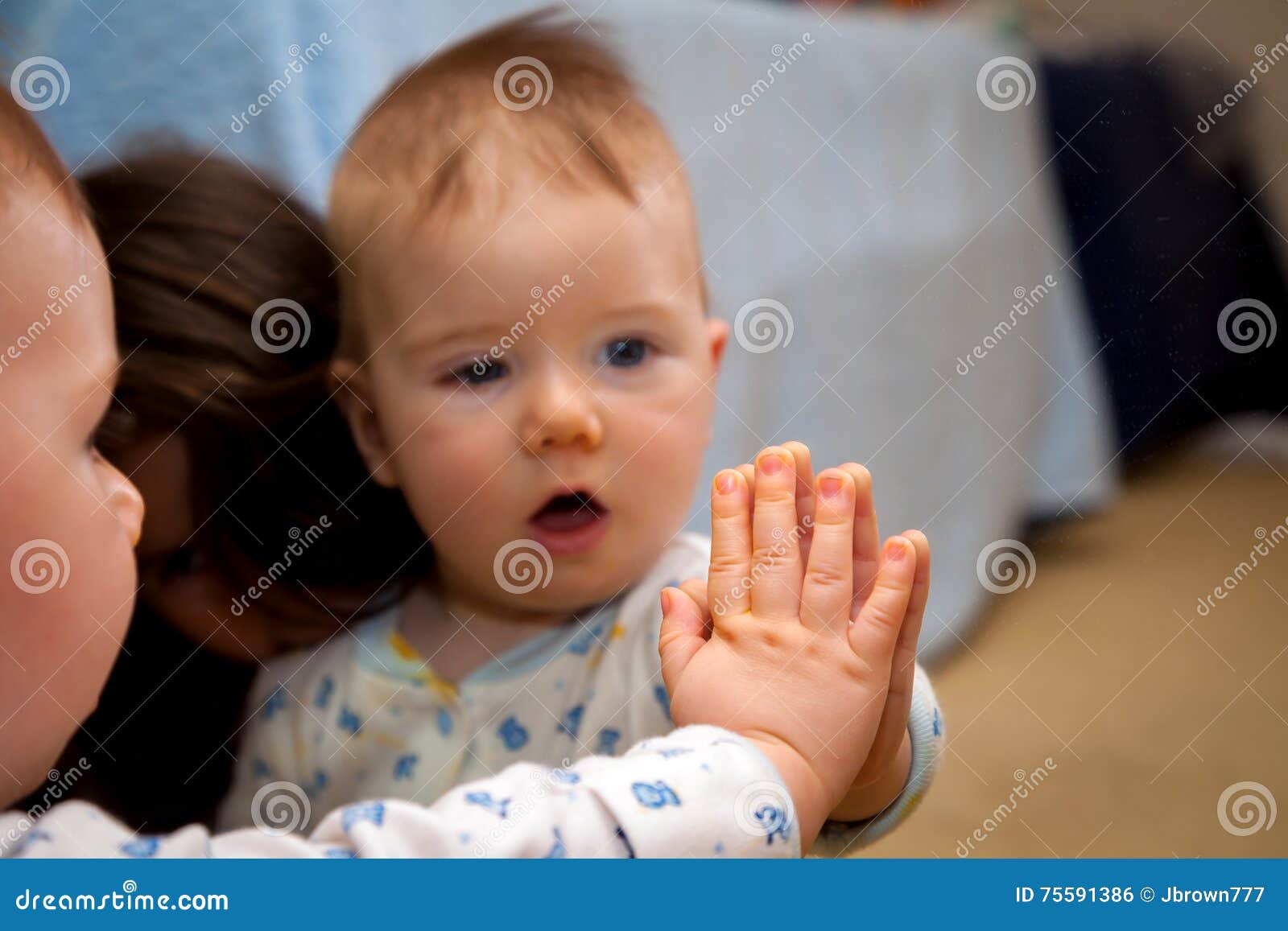 Il bambino tiene la sua mano su uno specchio ed è stupito dalla riflessione. Un bambino curioso tiene il suo tocco della mano fino a uno specchio ed osserva nella stupefazione la riflessione Sua sorella si siede accanto lui che si ammira