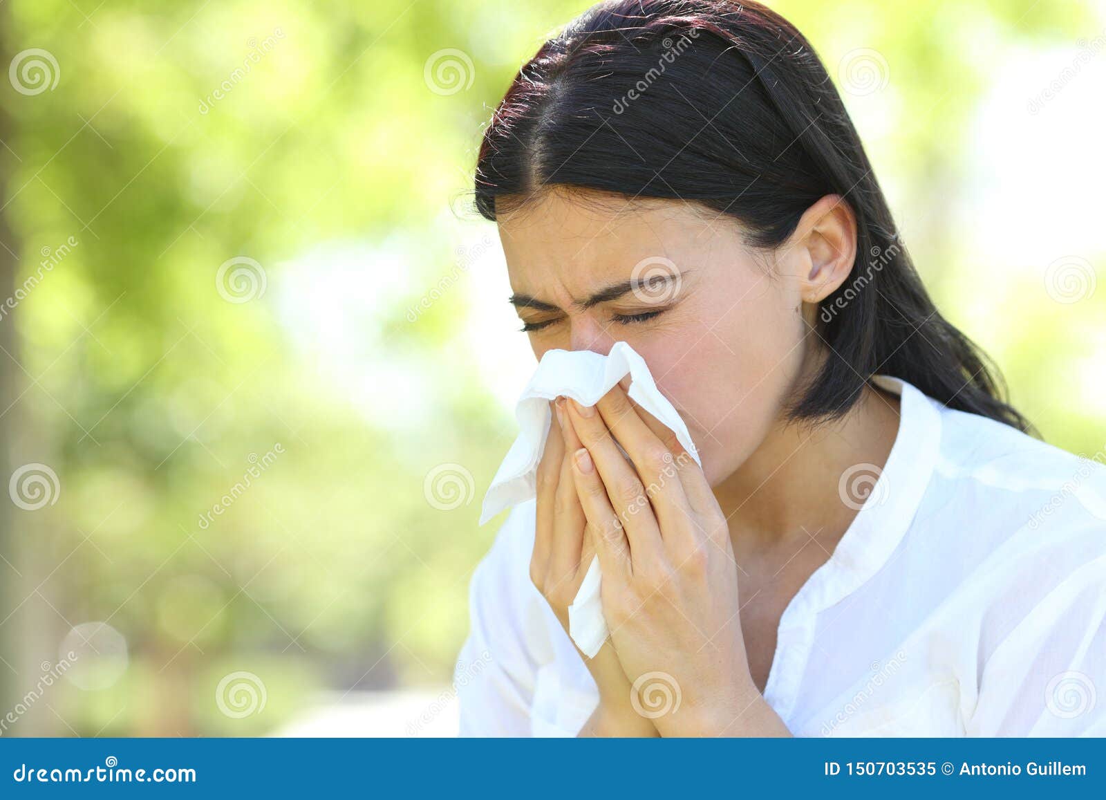 ill woman sneezing covering mouth with a wipe in a park