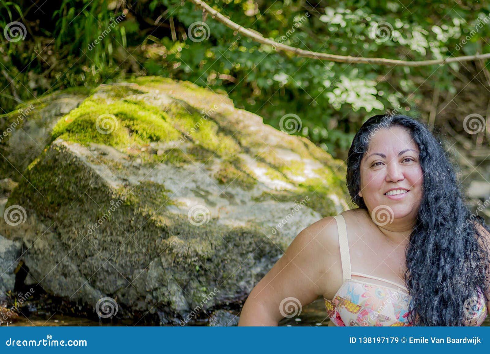 beautiful mexican woman smiling and looking at the camera with a big rock with moss in the background