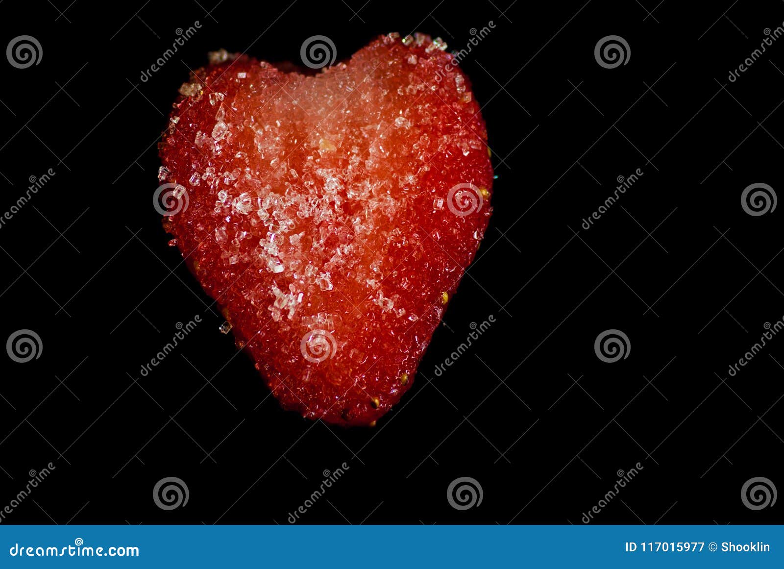 cut slice of a red juicy strawberry covered in sugar crystalls on a black background