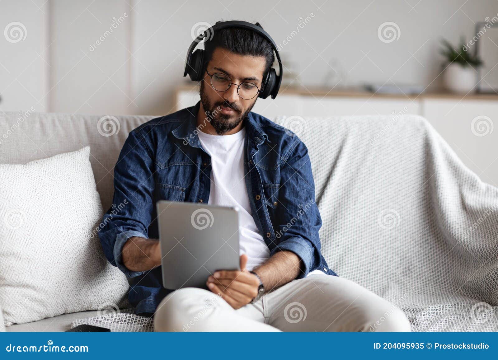 indian guy spending time at home with digital tablet and wireless headphones