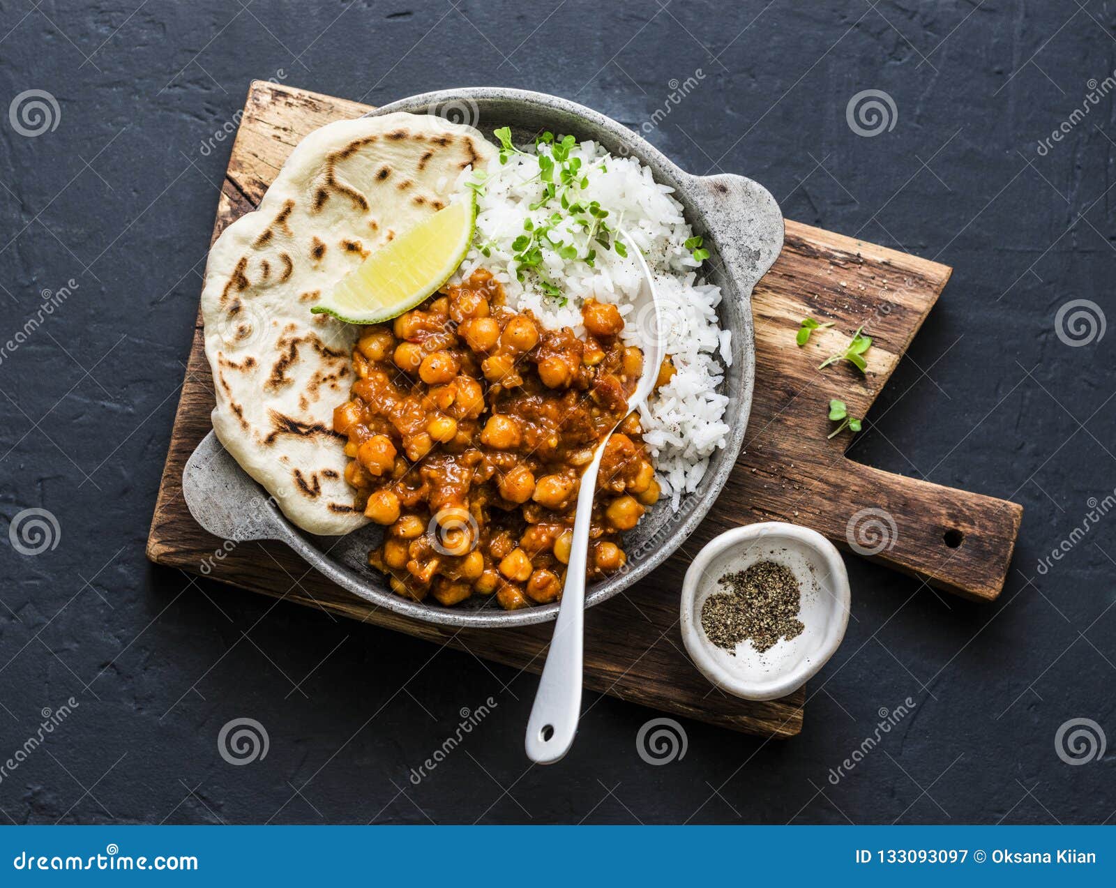 indian spicy chickpeas curry with rice and naan bread in pan on dark background, top view