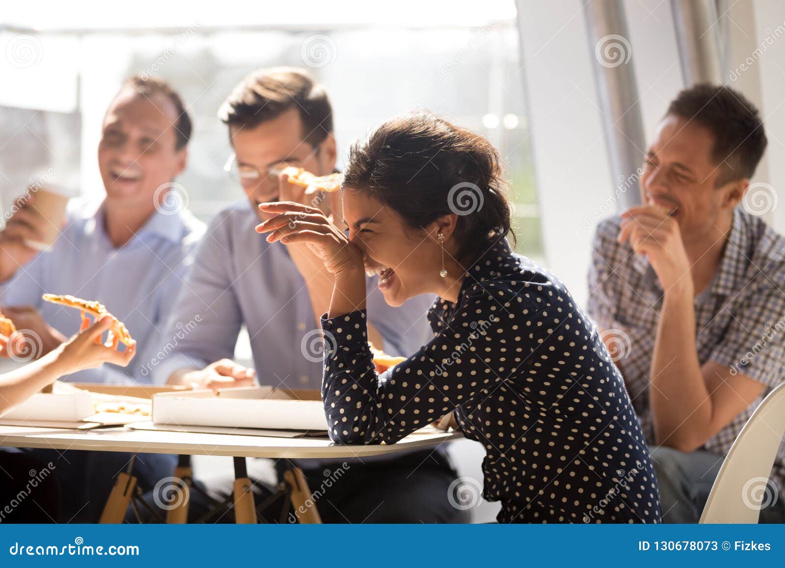 indian woman laughing eating pizza with diverse coworkers in off