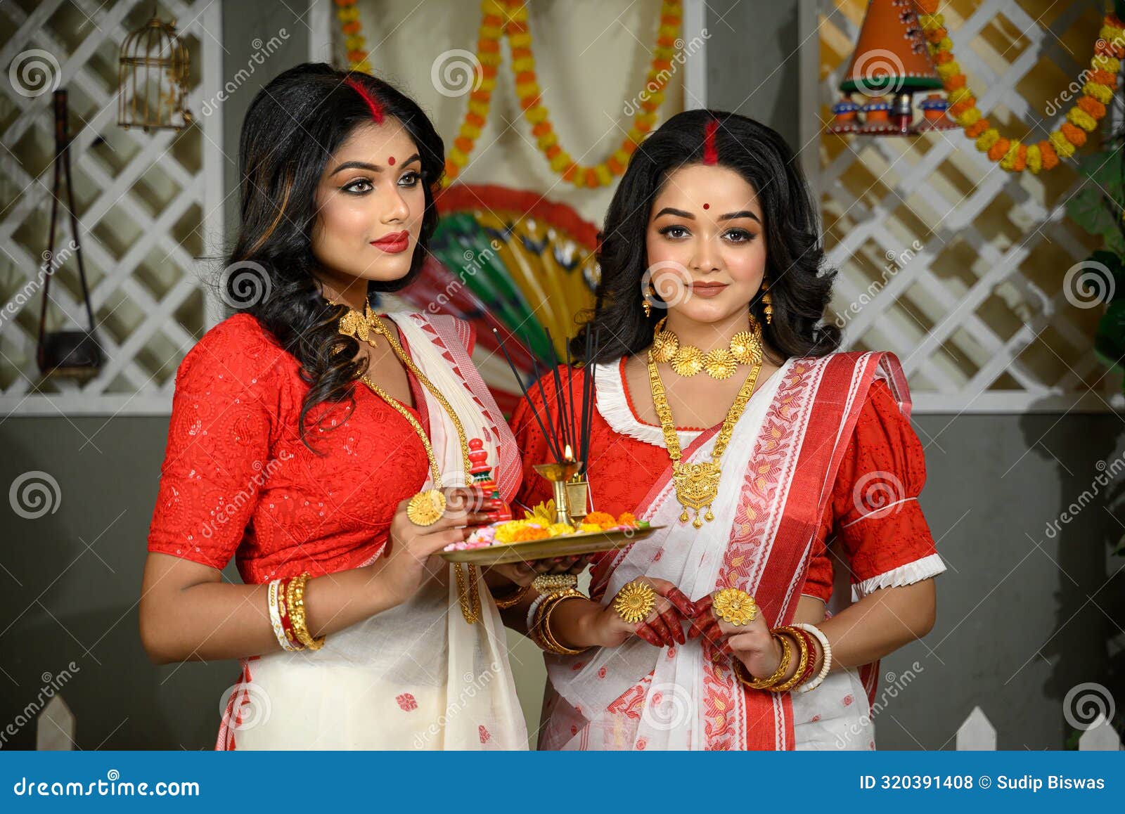 indian women, adorned in traditional sarees and gold jewellery, including bangles, holding a plate filled with religious offerings