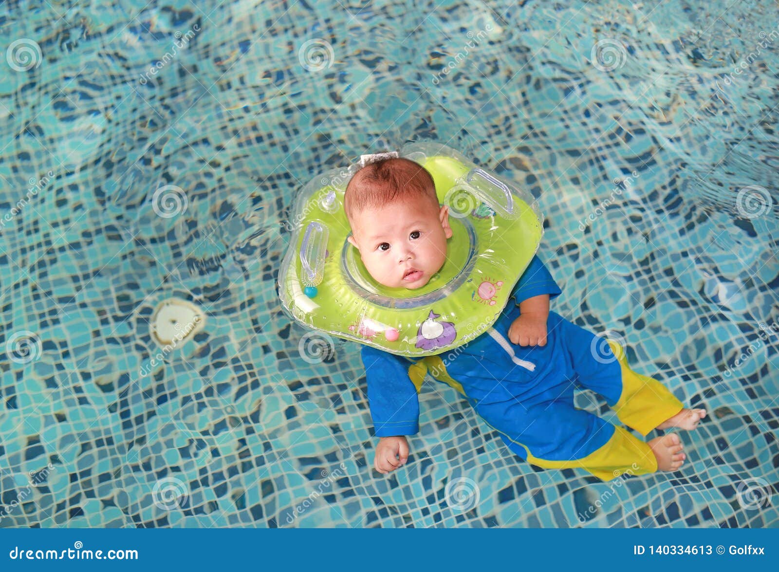 Infant baby boy training to swim in pool with safety by baby neck floats.