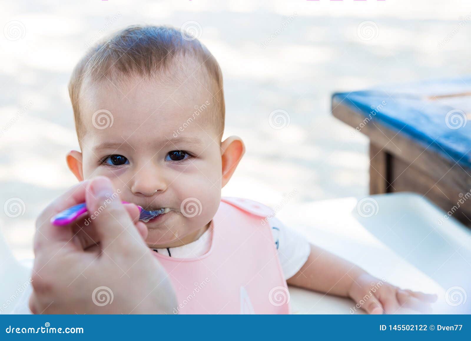 Infant Girl Eating Porridge With A Plastic Spoon On The Street Baby In