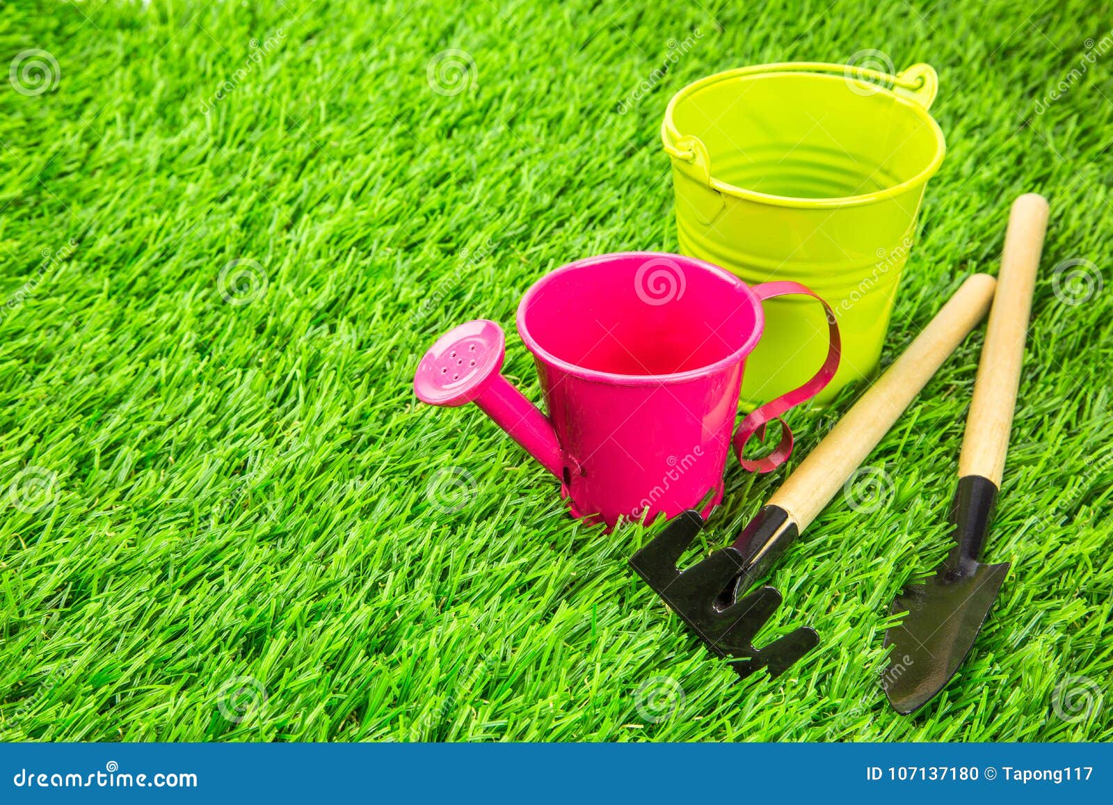 Piccoli innaffiatoio e strumenti di giardinaggio su erba artificiale come concetto di giardinaggio del fondo