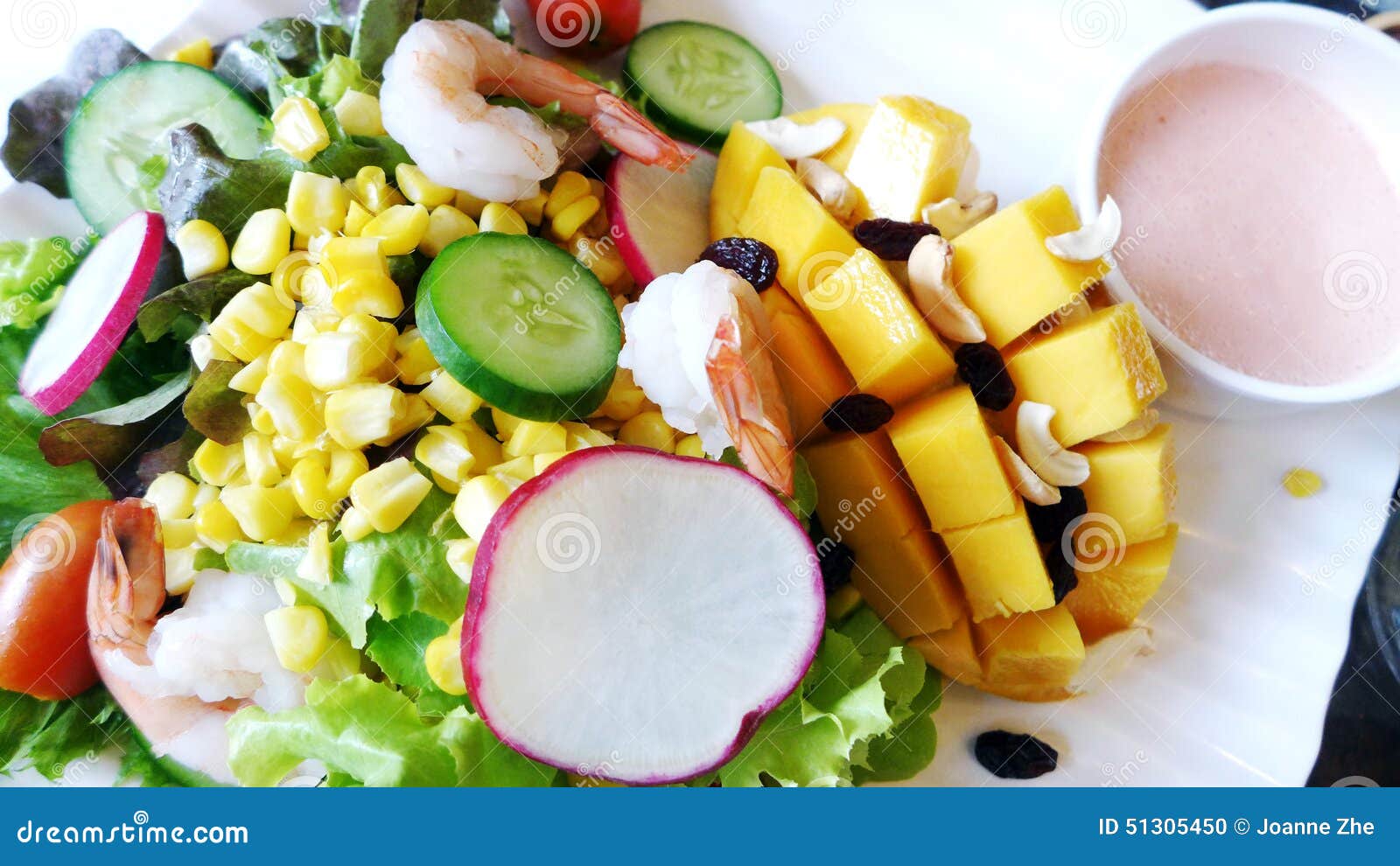 Insalata tropicale dei gamberetti del mango. Una fotografia che mostra un'insalata asiatica sudorientale tropicale deliziosa e sana di stile, fatta con i manghi, il mais, il cetriolo, la rapa, il ravanello, la lattuga, gli anacardi, le cipolle, i gamberetti e l'uva passa Servito dal lato con un succo della fragola ha basato il condimento delle insalate