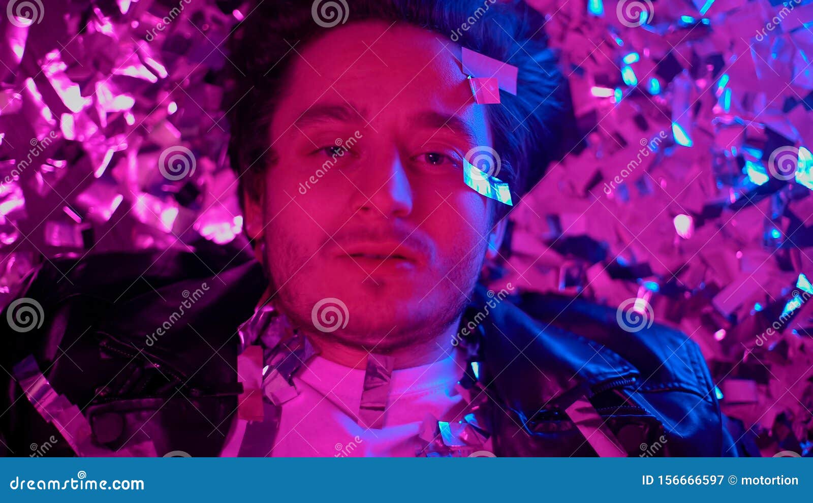 intoxicated man lying on floor among confetti and looking at camera, addict