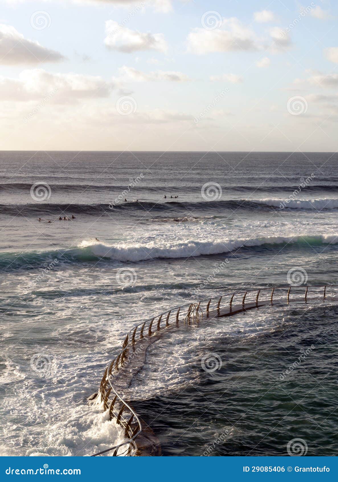 Iron railing in a sea with waves some people go surfing, is a vertical image