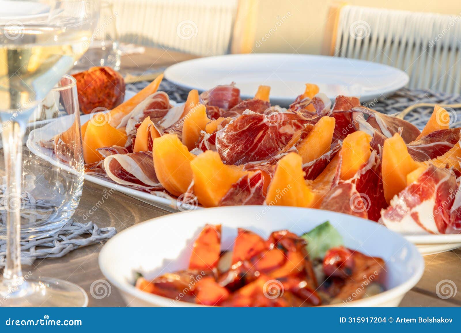 an italian alfresco dining setting, featuring a plate of prosciutto paired with sweet melon slices