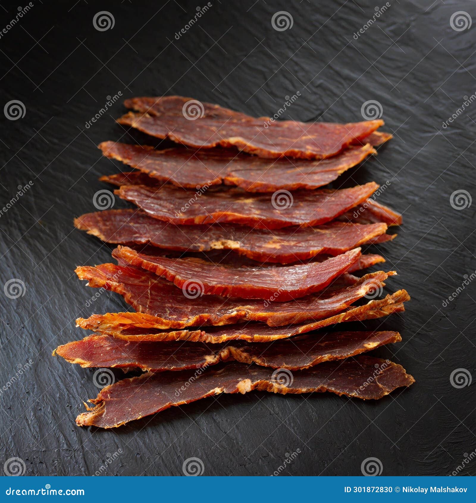 Jerky from Horse Meat or Beef on a Black Slate Background. Stock Photo