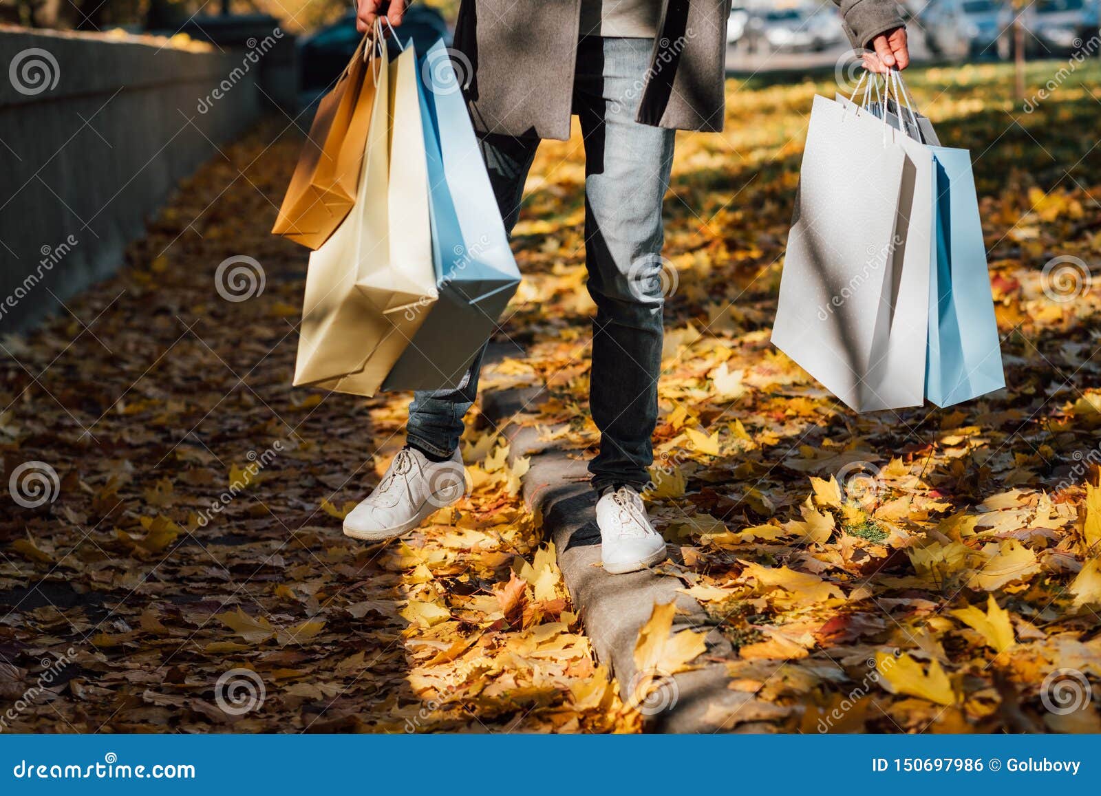 Jesieni zabawy mężczyzny toreb na zakupy spadek opuszcza chodniczek. Jesieni zabawa Cropped strzał mężczyzny odprowadzenie z torbami na zakupy, cieszy się sezon jesiennego z żółtymi liśćmi zakrywa chodniczek