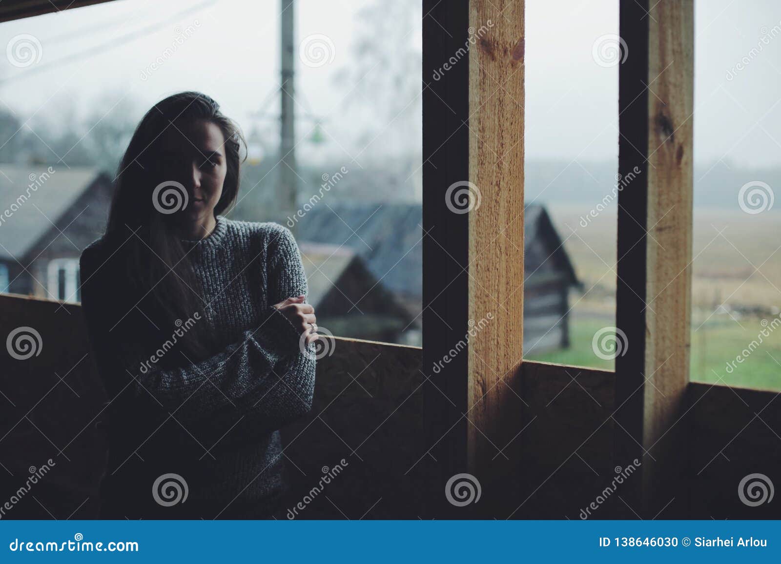 Jeune belle fille dans le village Modèle sur le fond d'une maison en bois dans le village Lumière foncée Fille caucasienne avec les cheveux foncés