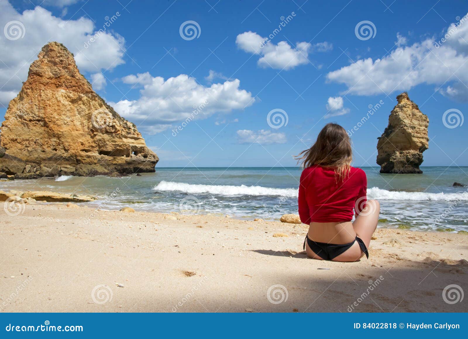 Jeune femme appréciant le jour parfait à la plage. Jeune fille s'asseyant dans le sable blanc sur la plage portant un petit bikini brésilien noir et une agrostide blanche