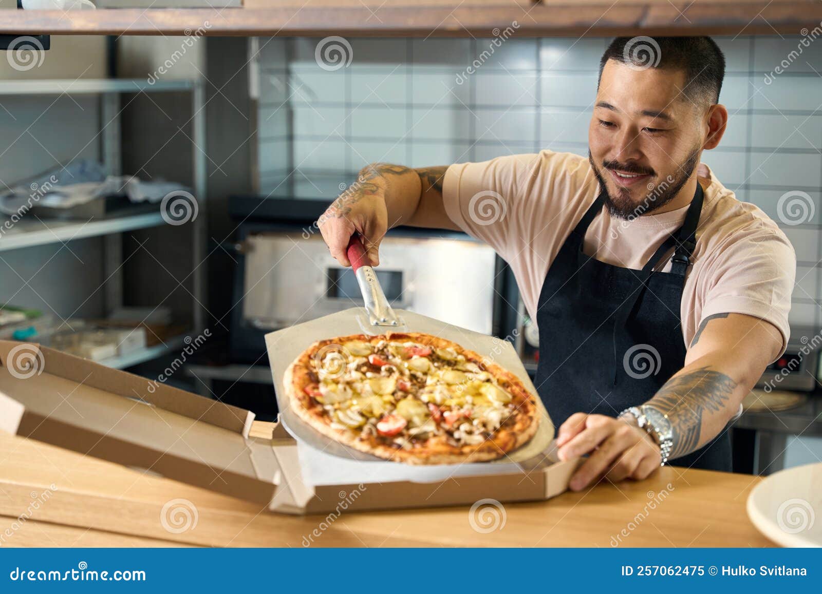 Jeune Homme Agréable Dans Le Tablier Cuisinier Emballer La Pizza Dans La  Boîte Image stock - Image du couches, fromage: 257062475