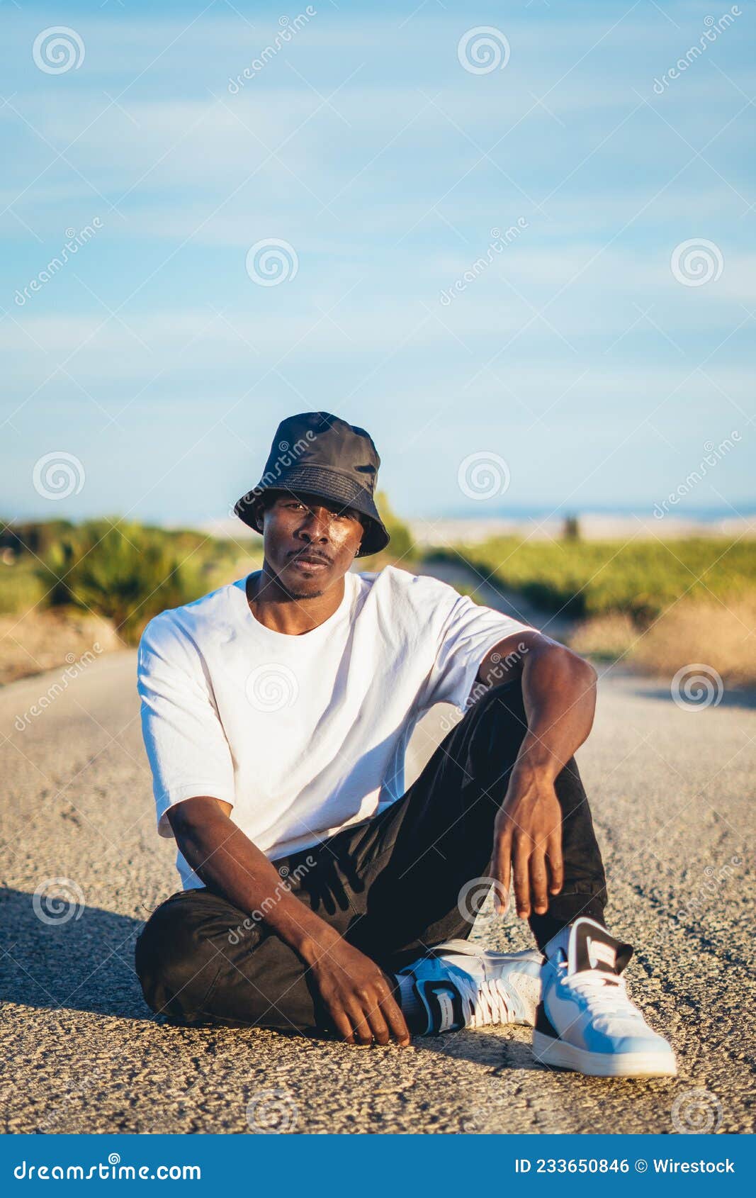 https://thumbs.dreamstime.com/z/jeune-homme-noir-et-beau-portant-un-chapeau-de-seau-assis-sur-le-sol-au-milieu-d-coucher-soleil-la-route-233650846.jpg