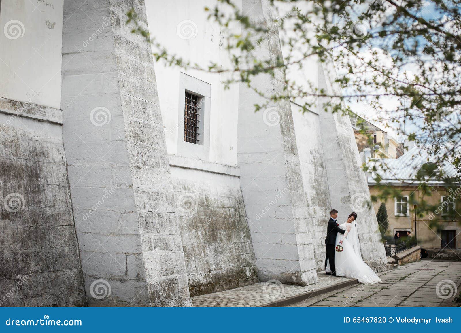 Jeune mariée magnifique de brune étreignant le marié et posant près du vieux mur de château