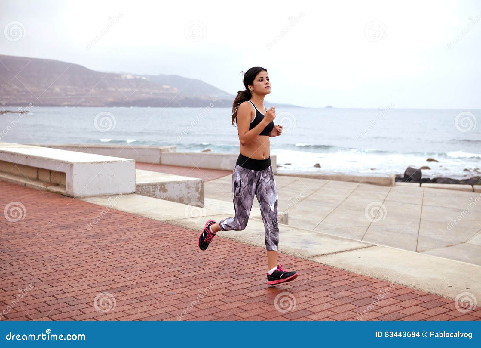 Jeune taqueur femelle sur l'esplanade. Jeune fille pulsant sur une esplanade pavée près d'un bord de la mer, des vêtements sport de port, des chaussures de course et de ses cheveux attachés de retour