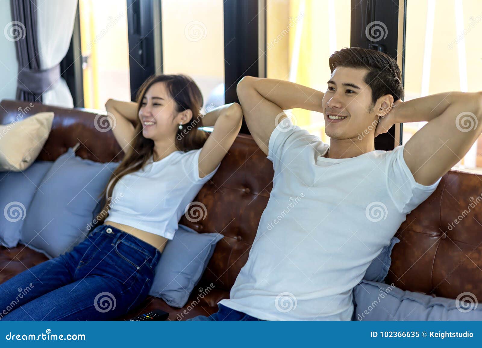 Jeunes couples asiatiques décontractés dans le moment doux et le televisi de observation. Jeunes couples asiatiques décontractés dans le moment doux et télévision de observation dans le salon lumineux