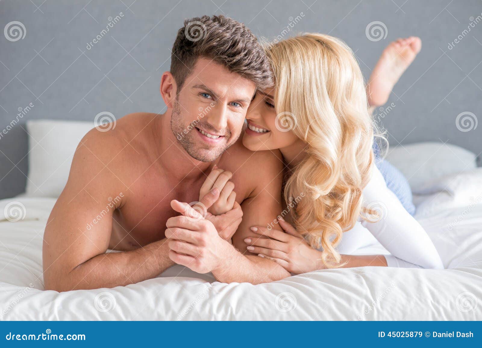Jeunes couples sexy des moments de bonbon à lit. Jeunes couples doux sexy se trouvant sur la pousse blanche de mode de lit D'isolement sur le fond gris