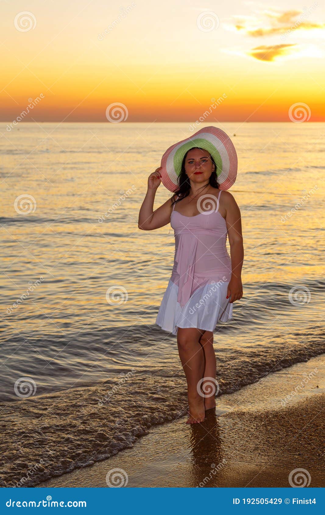 a jewish woman in a hat and white dress at sunset walks along the seashore.