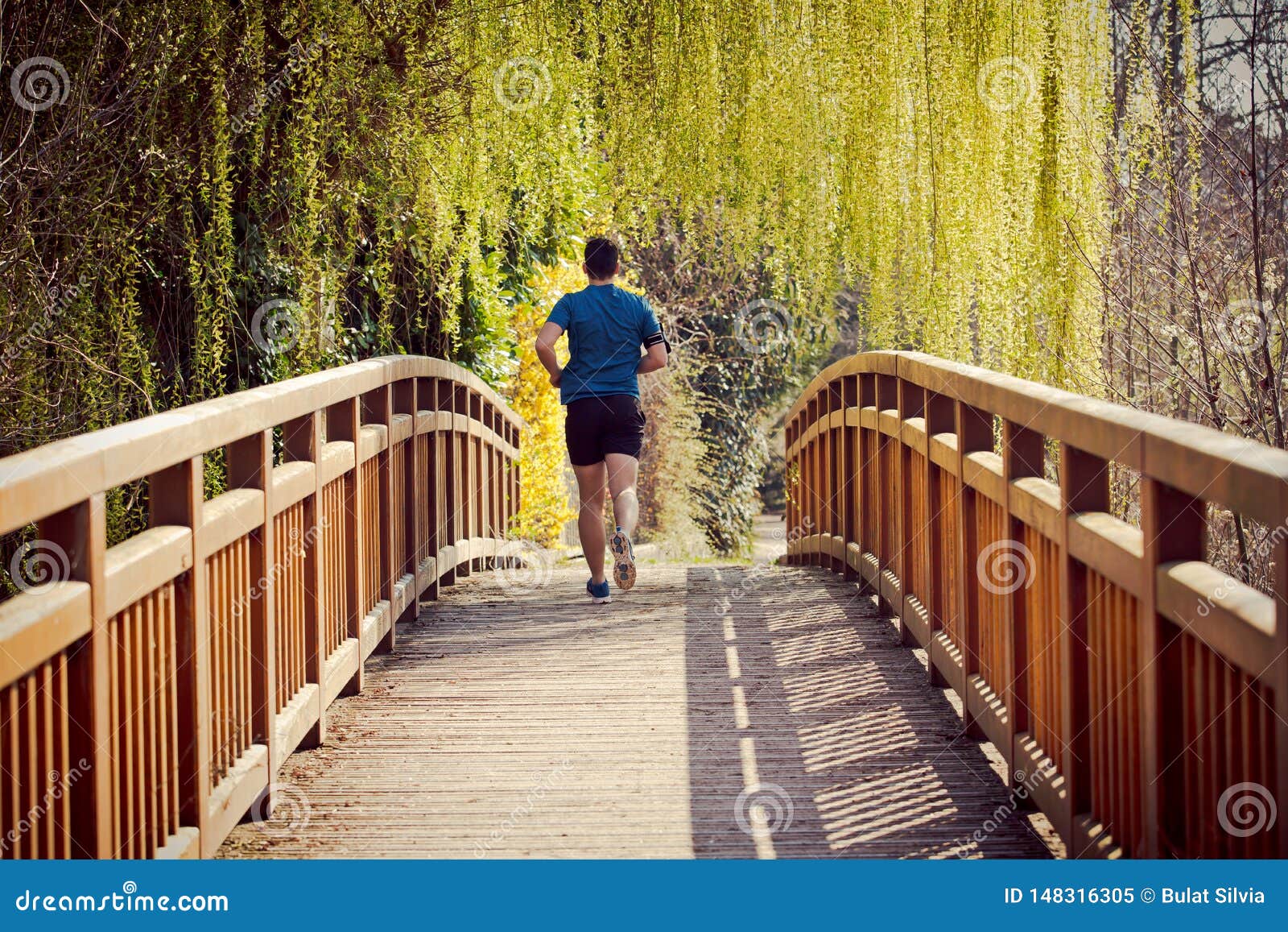 Rear view Male runner running in a city park over bridge training for fitness. Healthy lifestyle concept. Workout jogging activity, dynamic runner athlete