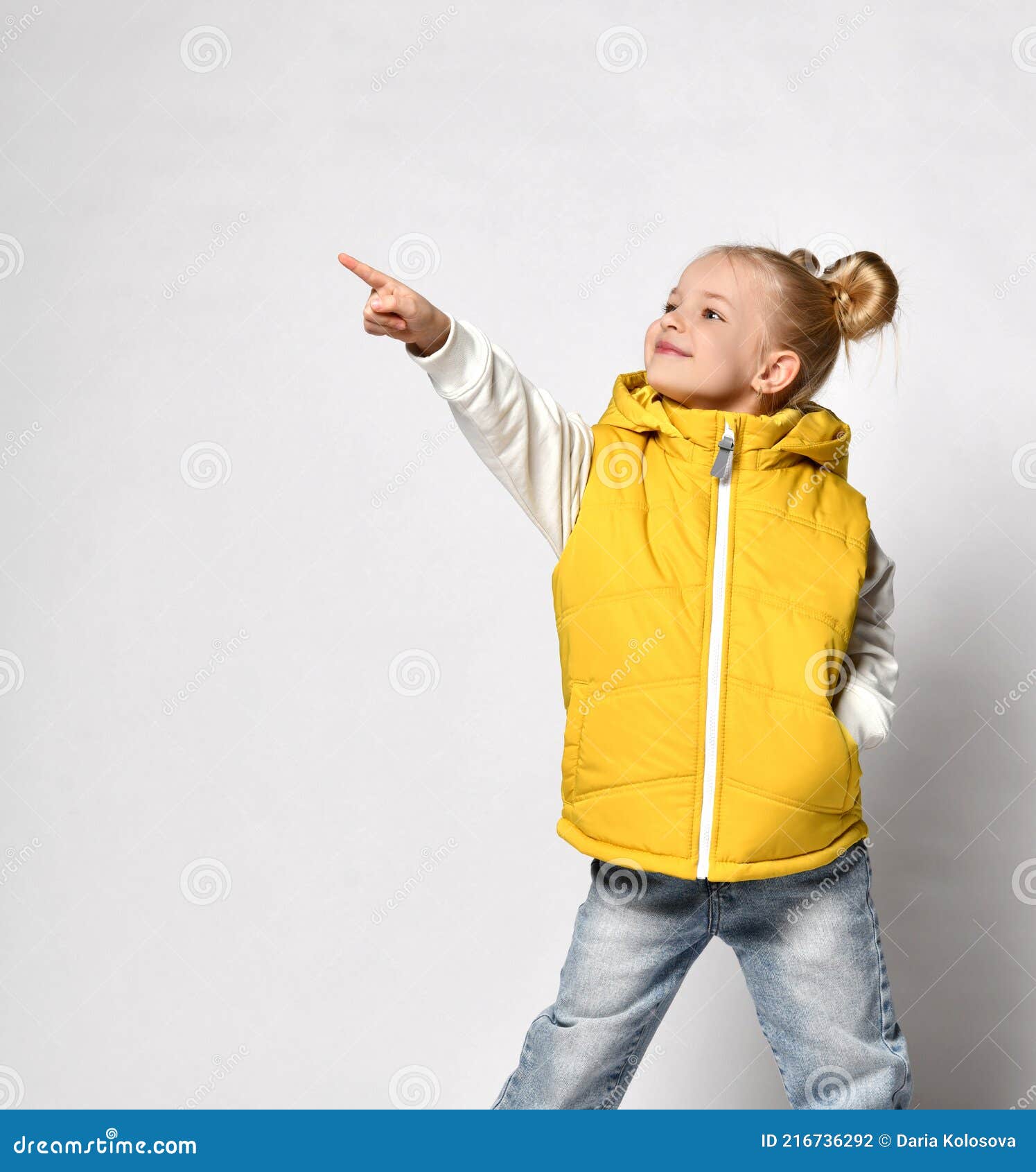 Jolie Fille Blonde Souriante Dans Un Gilet Jaune Bouffi Est Debout Avec Sa Main Dans Sa Poche Et Pointant Avec Son Autre Photo stock Image du masculin capot 216736292