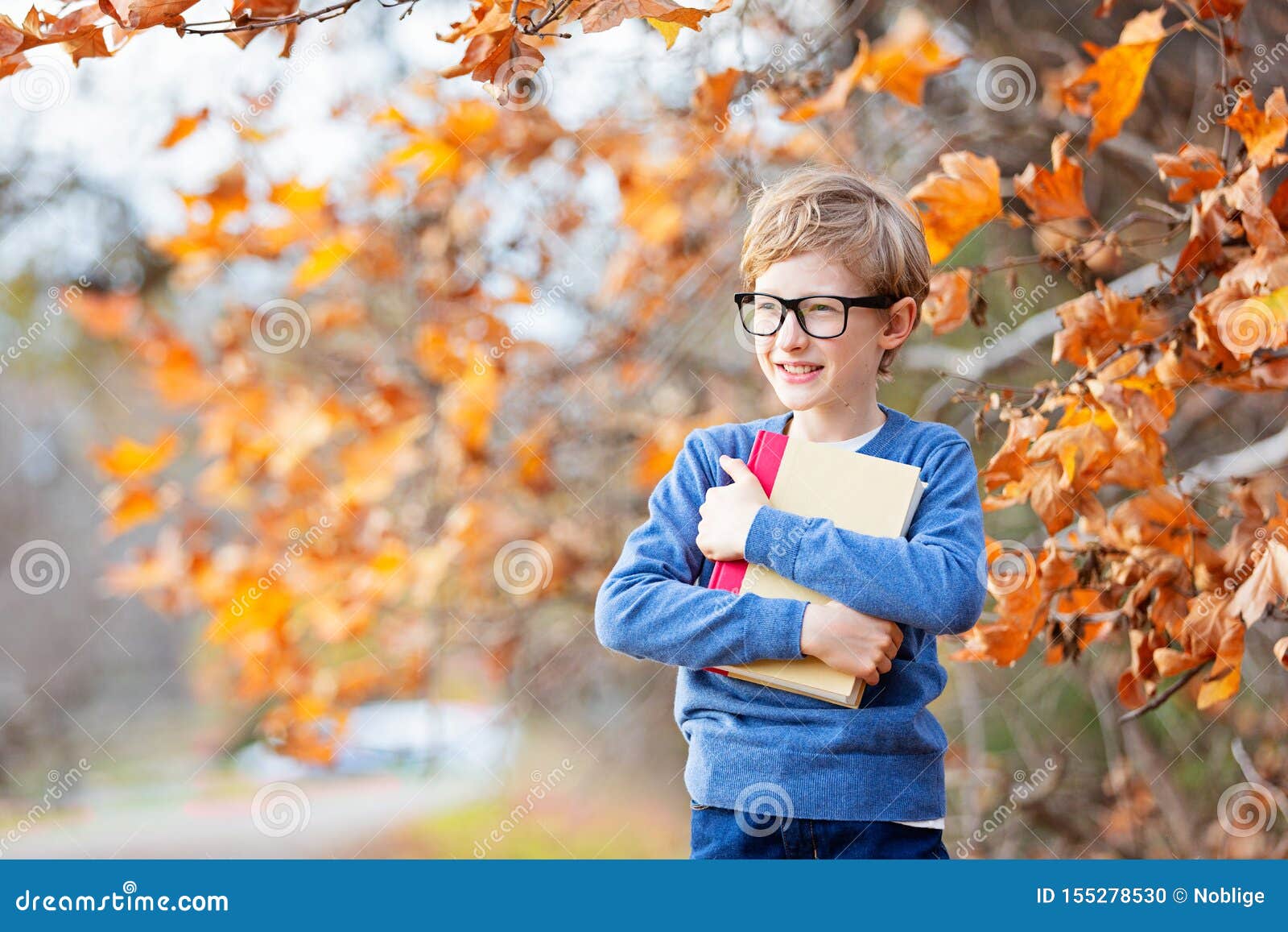 Jong geitje bij daling. Positieve glimlachende jongen die in glazen boek houden voor een nieuw schooljaar, terug naar schoolconcept, dalingstijd in het park, exemplaarruimte klaar op linkerzijde