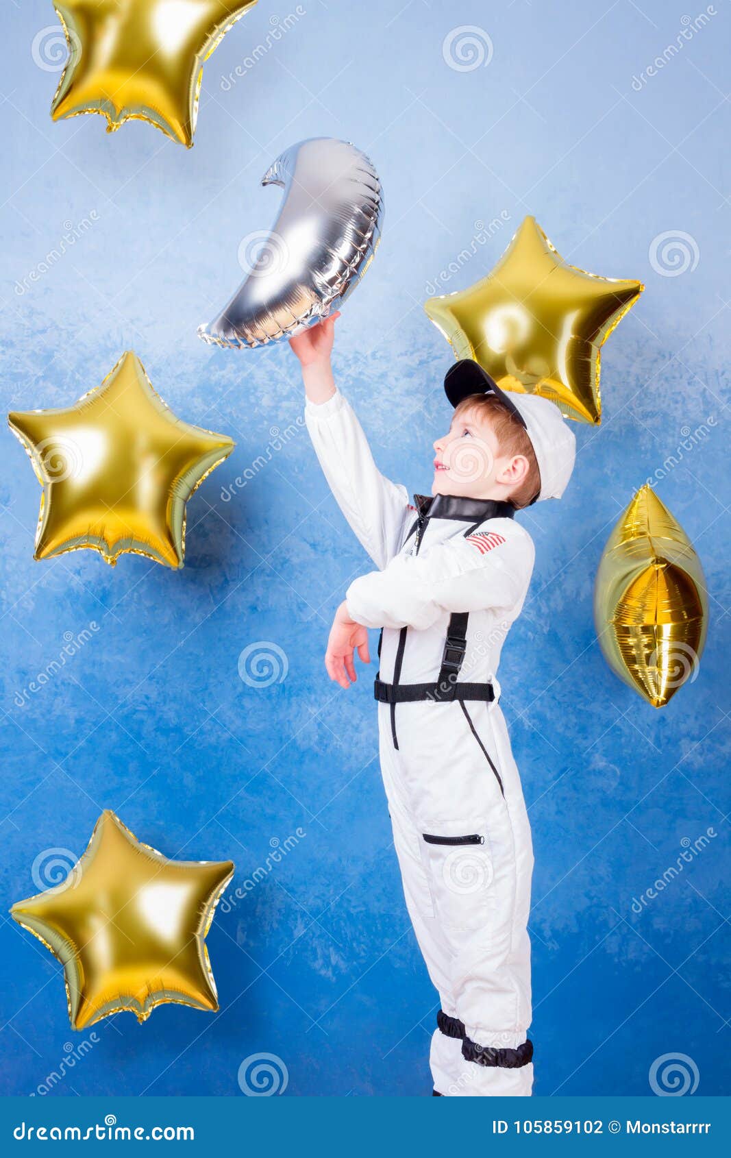 Jong geitje het spelen in astronaut met maan. Jong kindjongen het mannelijke spelen in astronaut met zilveren maan in wit astronautenkostuum en het dromen over het vliegen in kosmos door de sterren die dichtbij gouden ster` s ballons blijven op blauwe achtergrond