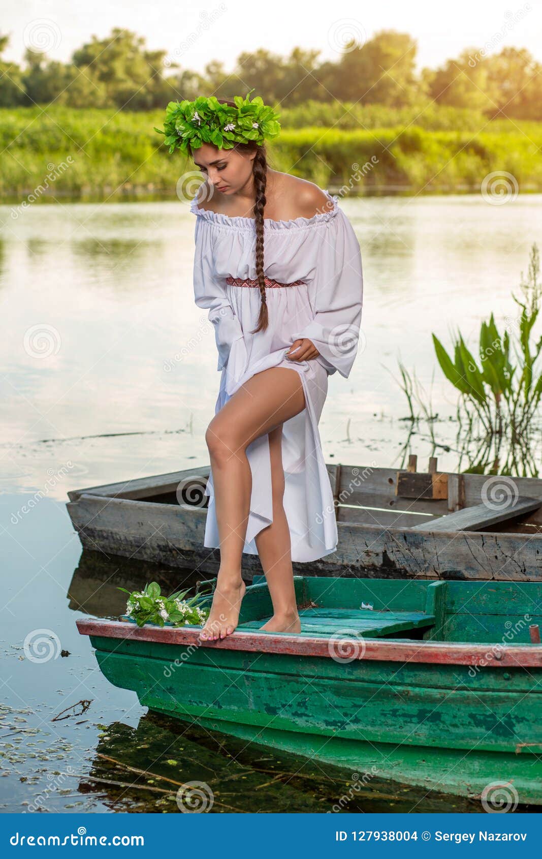 Jonge sexy vrouw op boot bij zonsondergang Het meisje heeft een bloemkroon op haar hoofd die, die en op rivier ontspannen varen a. Jonge sexy vrouw op boot bij zonsondergang Het meisje heeft een bloemkroon op haar hoofd die, die en op rivier ontspannen varen Mooi lichaam en gezicht De fotografie van de fantasiekunst Concept vrouwelijke schoonheid, rust in het dorp