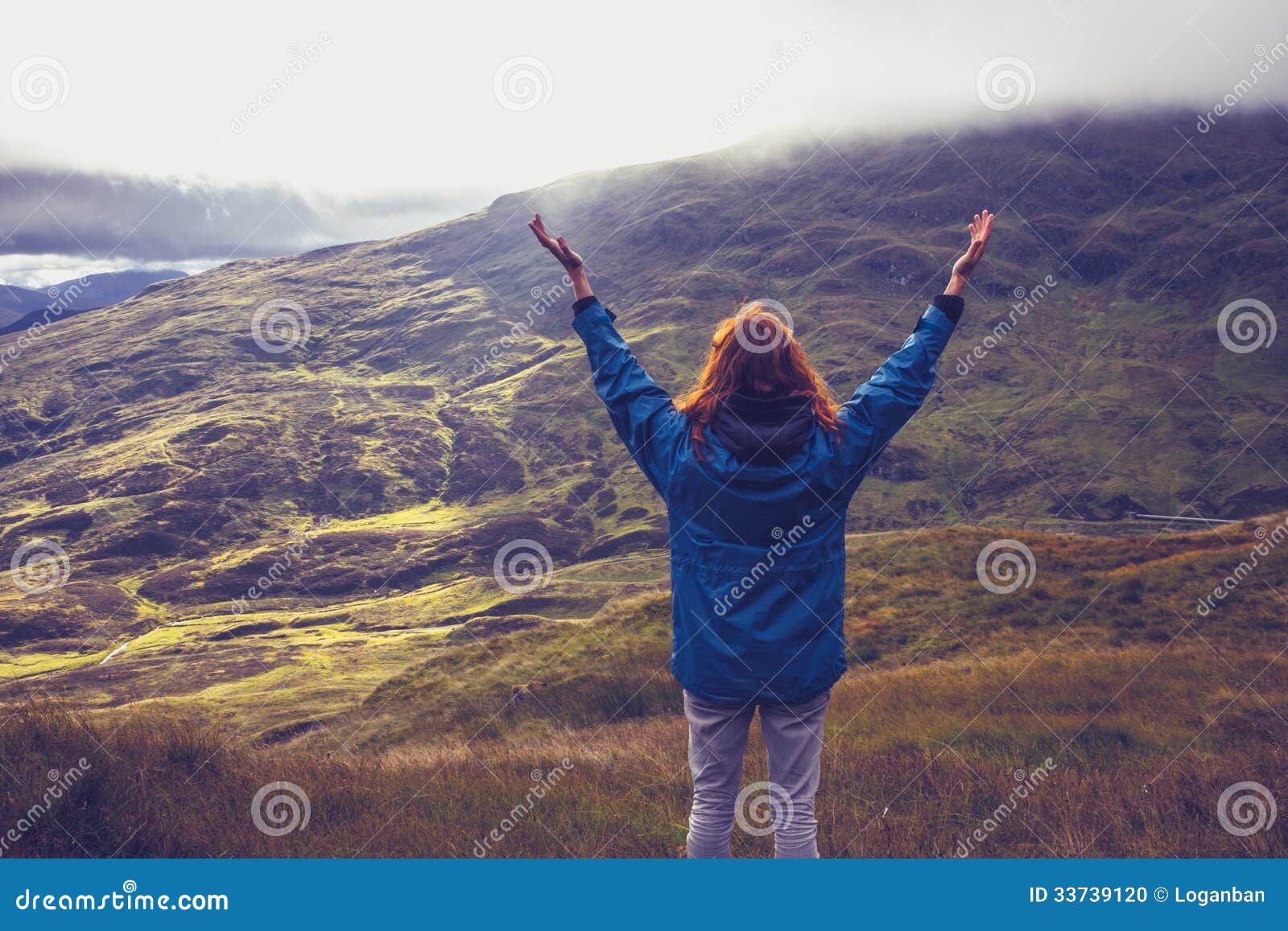 Jonge vrouw die met aard op bergbovenkant zijn. De jonge vrouw rekt uit haar wapens uit en is met aard op een bergbovenkant