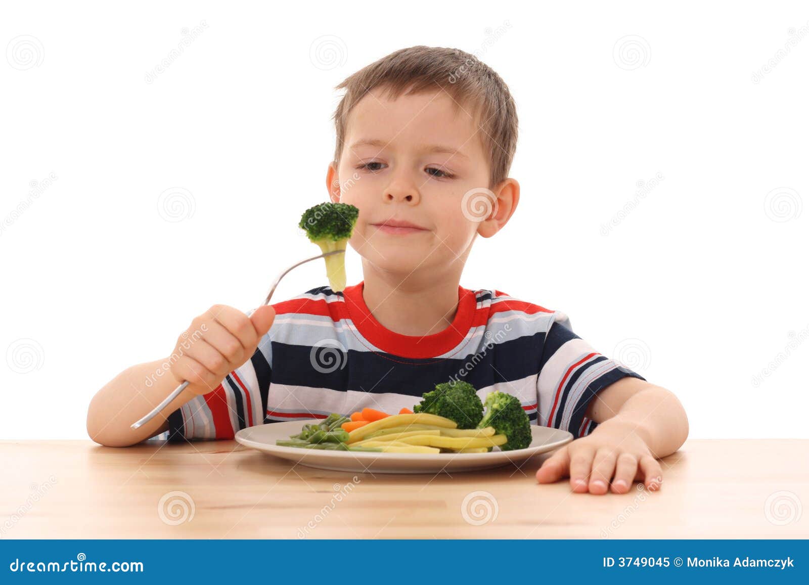Jongen en gekookte groenten. 5-6 jaar oude jongen en plaat van gekookte groenten die op wit worden geïsoleerds