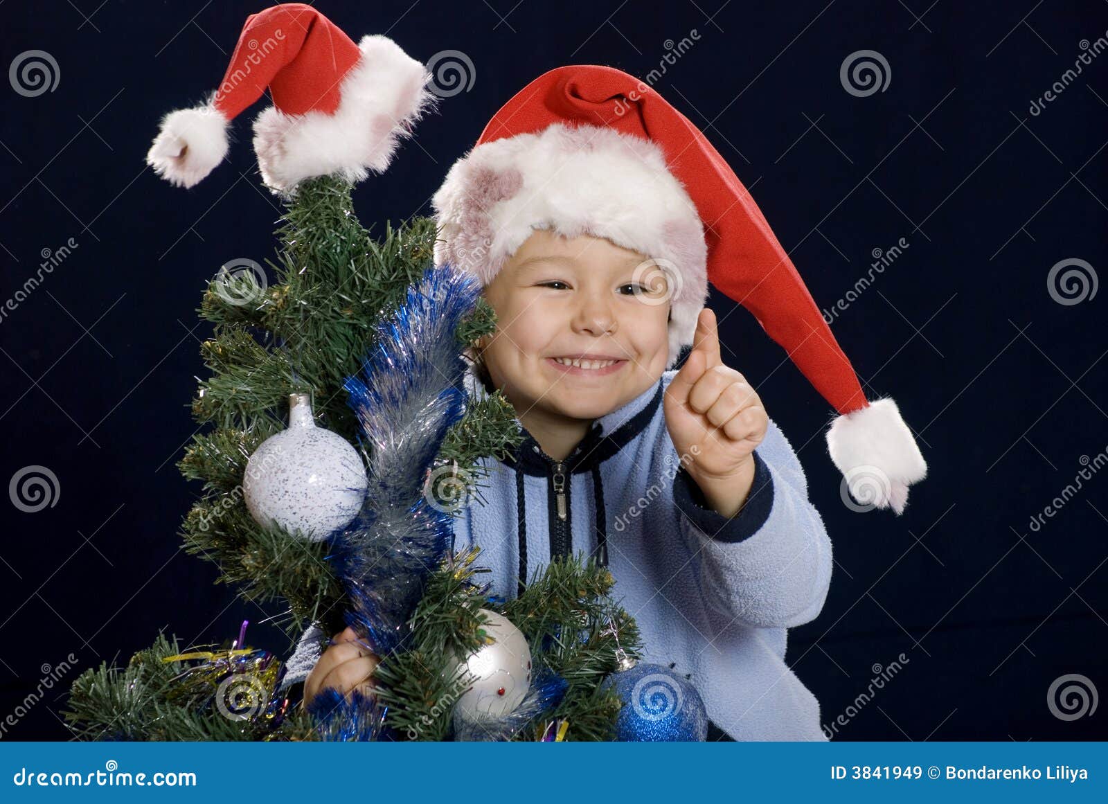 Jongen op de vakantie van Kerstmis om vinger op te heffen. Weinig jongen in een rood GLB met een aantal Kerstbomen om vinger op te heffen