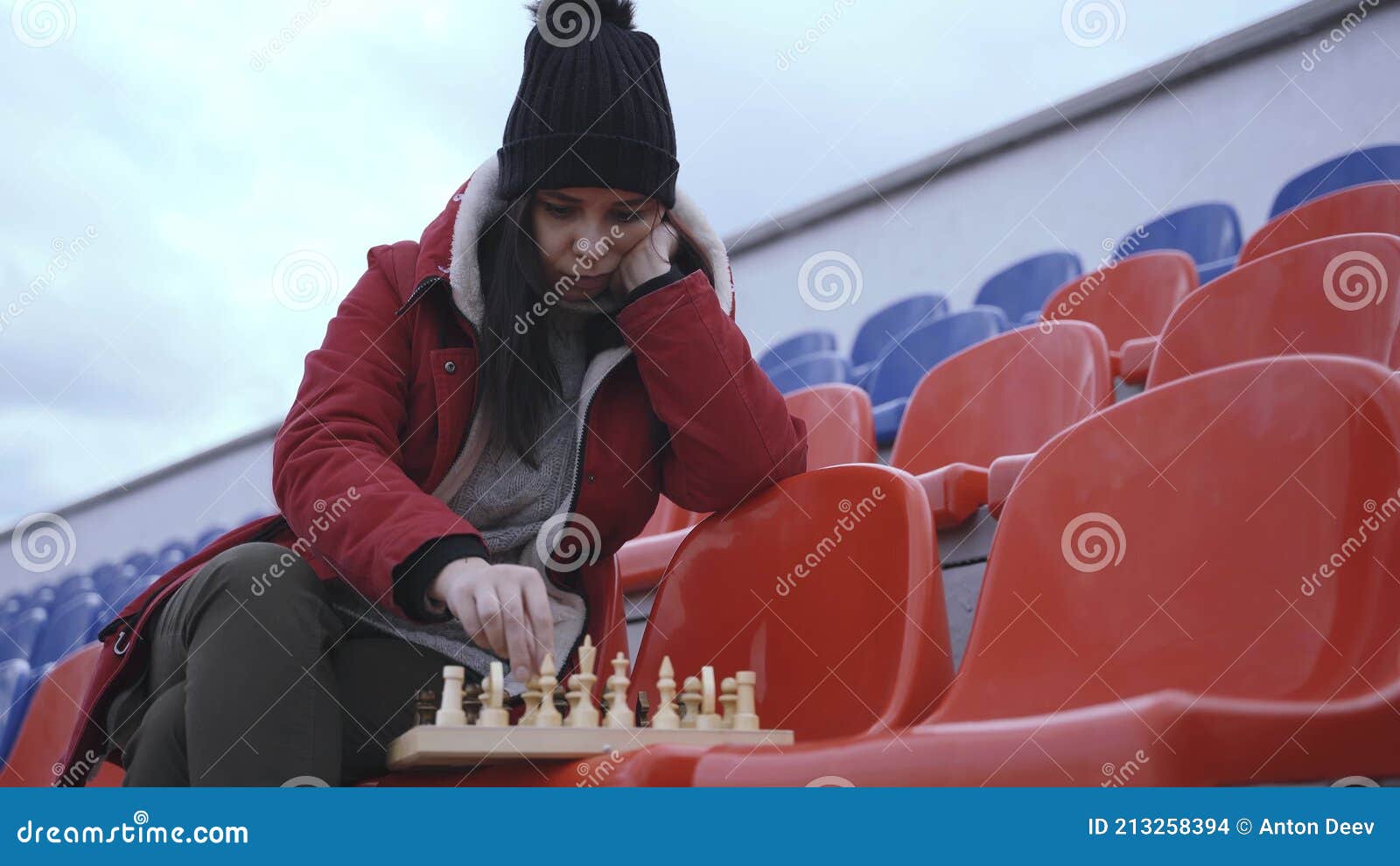 Jovem em roupas de inverno joga xadrez sentado nas arquibancadas