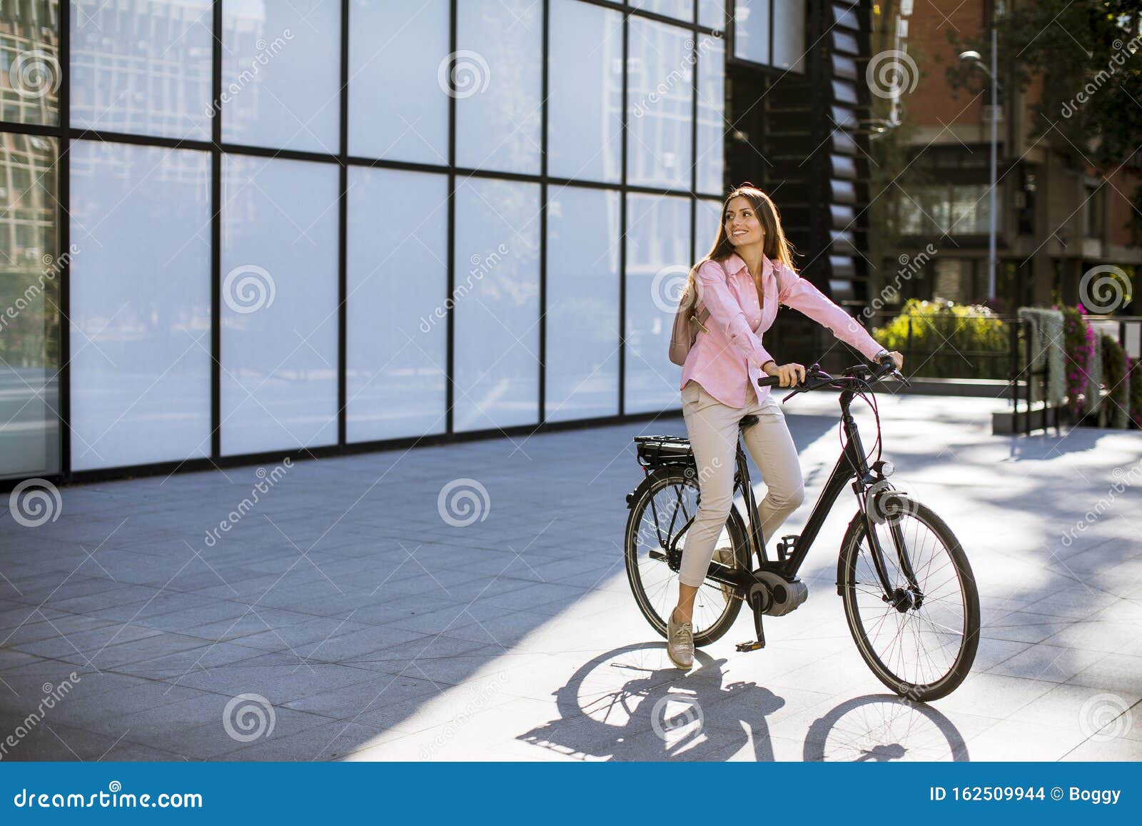 Mujer joven montando una bicicleta eléctrica y utilizando el teléfono móvil