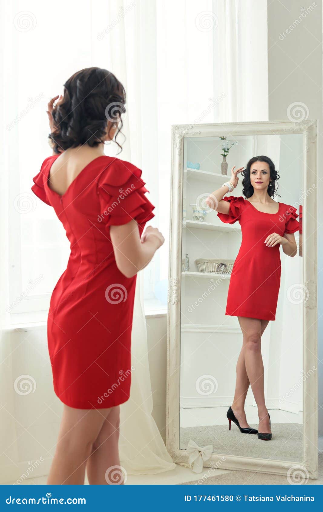 Joven Morena Mujer De Pie Mirando Con Reflexión En Un Espejo De Cuerpo Entero Con Un Vestido Rojo Corto Y Tacones Foto de archivo - Imagen longitud: