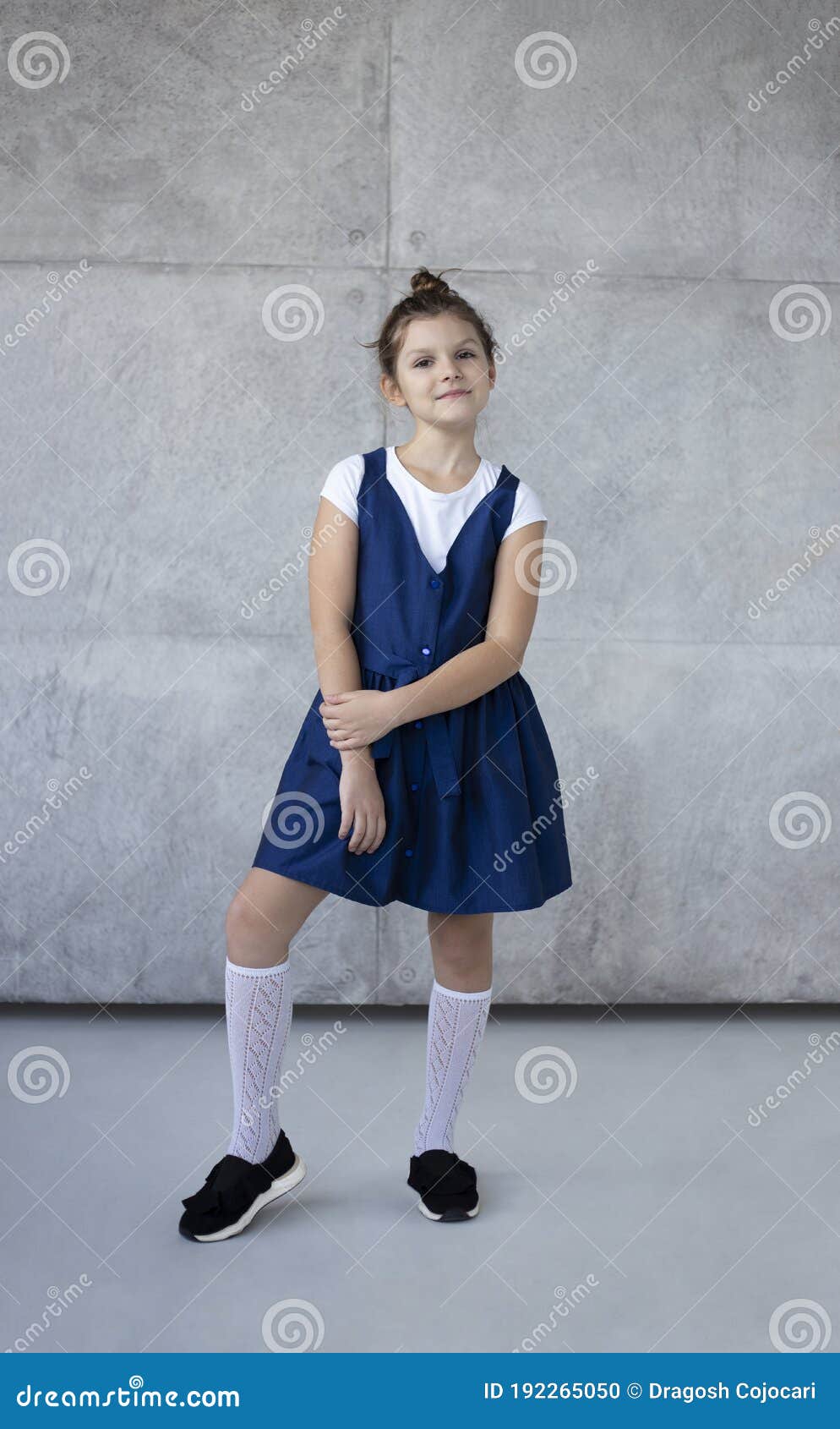 Joven Niña De Escuela De Diversión Con Camisa Blanca Y Uniforme Azul Sobre Fondo Hormigón Niños Retrato De Estudio Foto de archivo - Imagen de concreto, gente:
