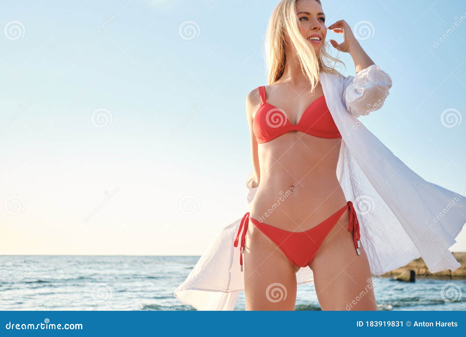 Joven Y Hermosa Rubia Con Traje De Baño Y Camisa Blanca Que Mira Soñadoramente a Un Lado De La Playa Con El Mar En Segundo P Imagen de archivo - Imagen