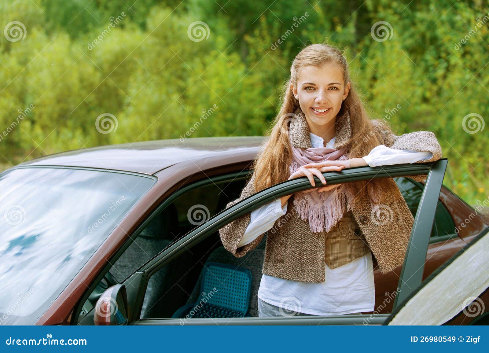 Jovens bonitos de sorriso. Retrato do mulher-excitador novo bonito de sorriso perto do carro, de encontro ao fundo do parque do outono.
