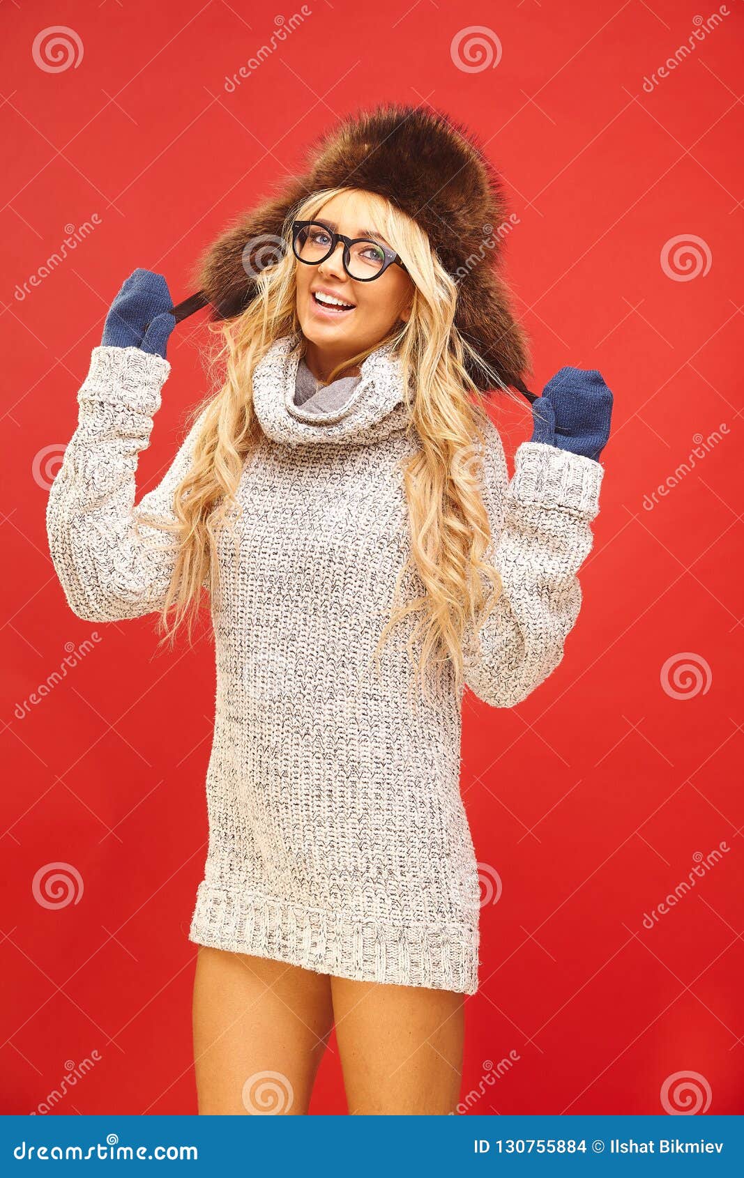 joy woman in ushanka hat, wears white turtleneck sweater, looks into camera, expresses her satisfaction,  on red