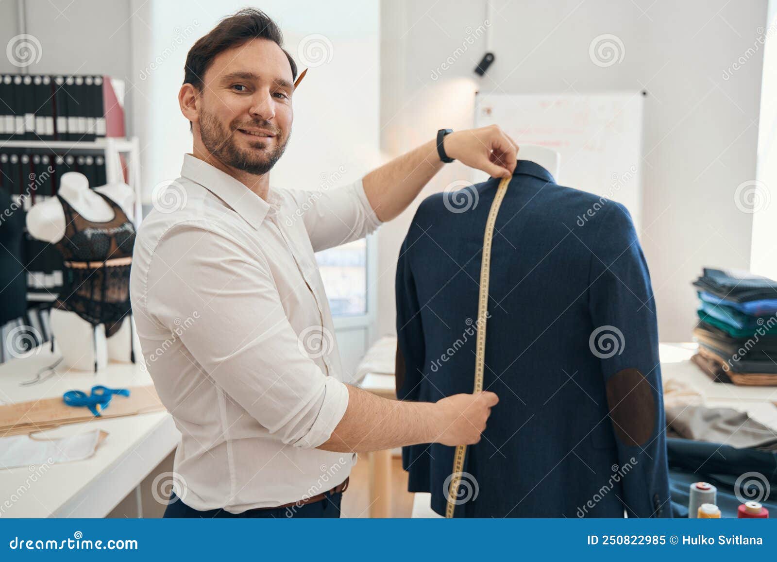 man couturier measures ength of jacket on a mannequin