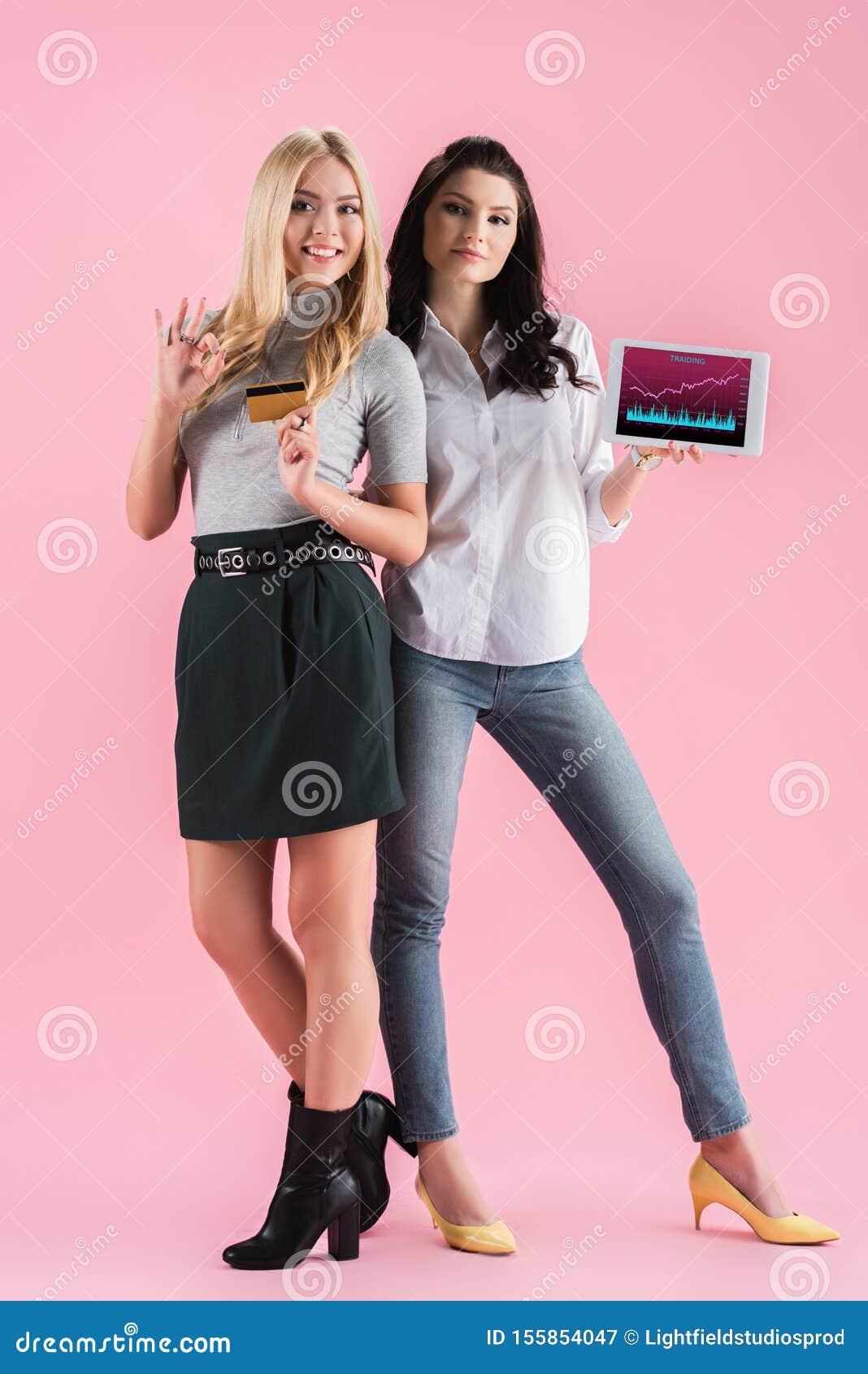 joyful girls holding digital tablet with traiding app on screen and credit card