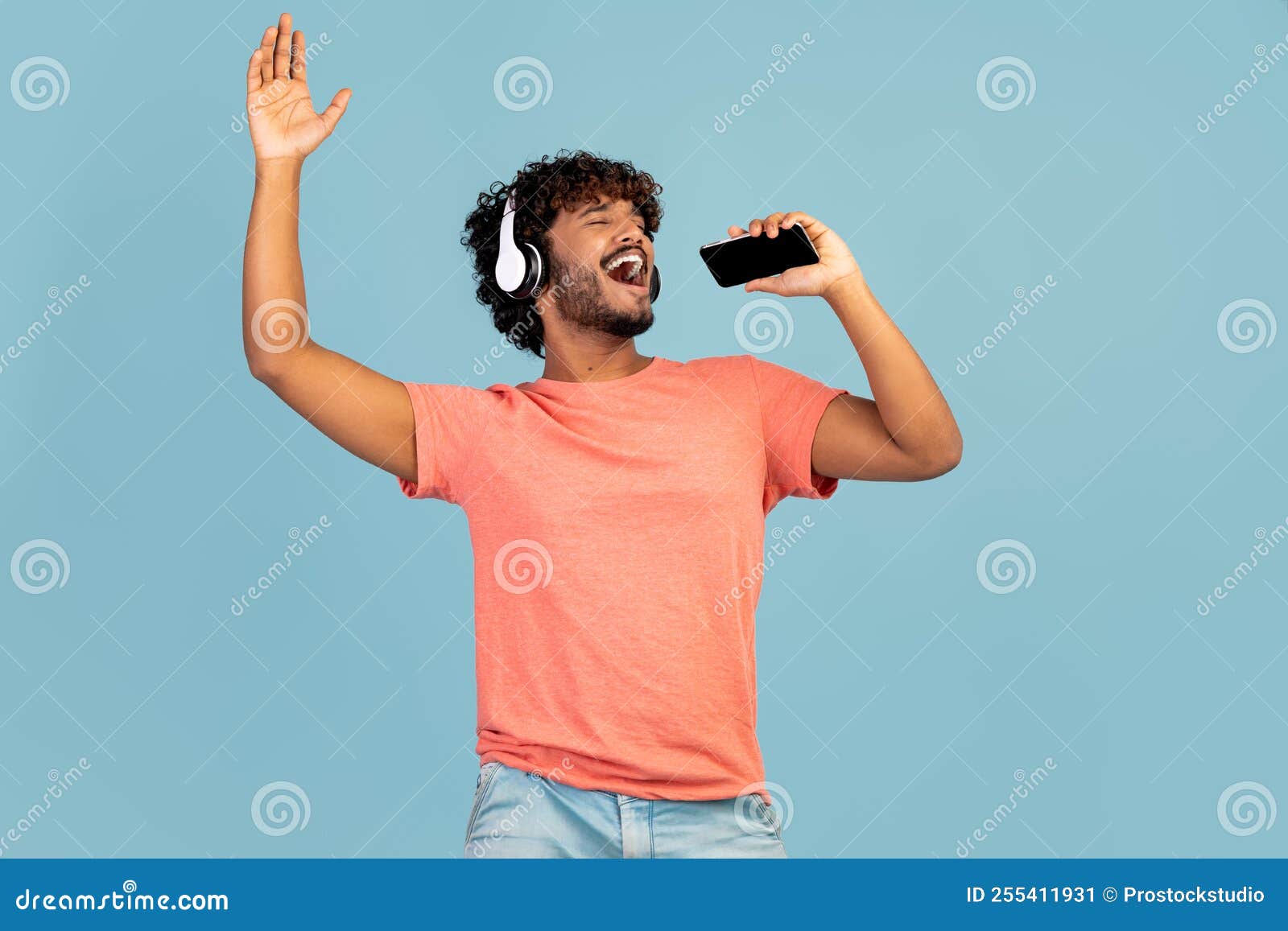 Joyful Indian Guy Singing Karaoke, Using Smartphone and Headset Stock