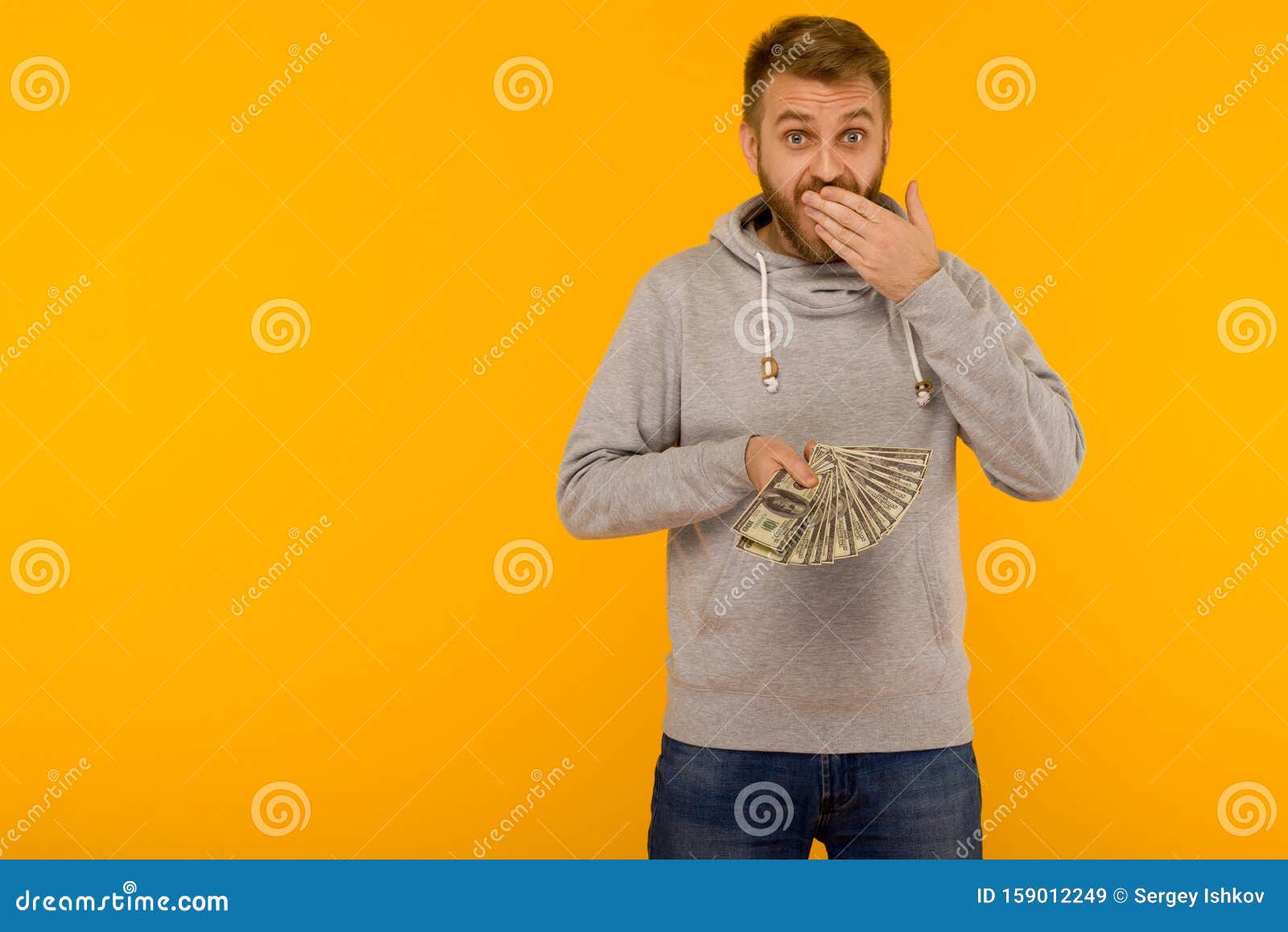 Joyful Man in a Gray Hoodie Holds Money Dollars Covering His Mouth with ...